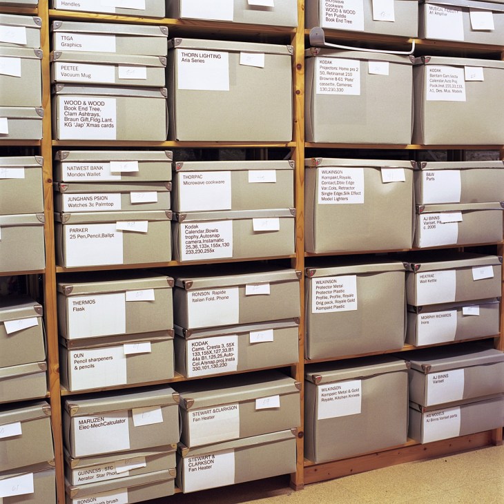 Wooden shelving unit with labeled drawers containing archived design files and product samples from Kenneth Grange's studio.
