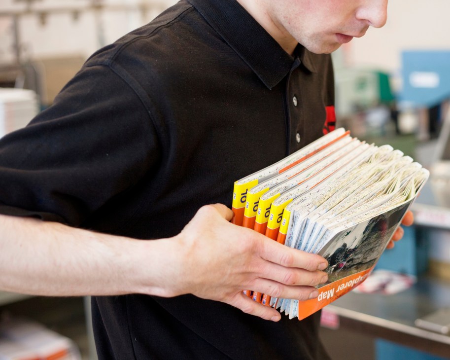 Worker holding a stack of Ordnance Survey maps with orange spines ready for packing.