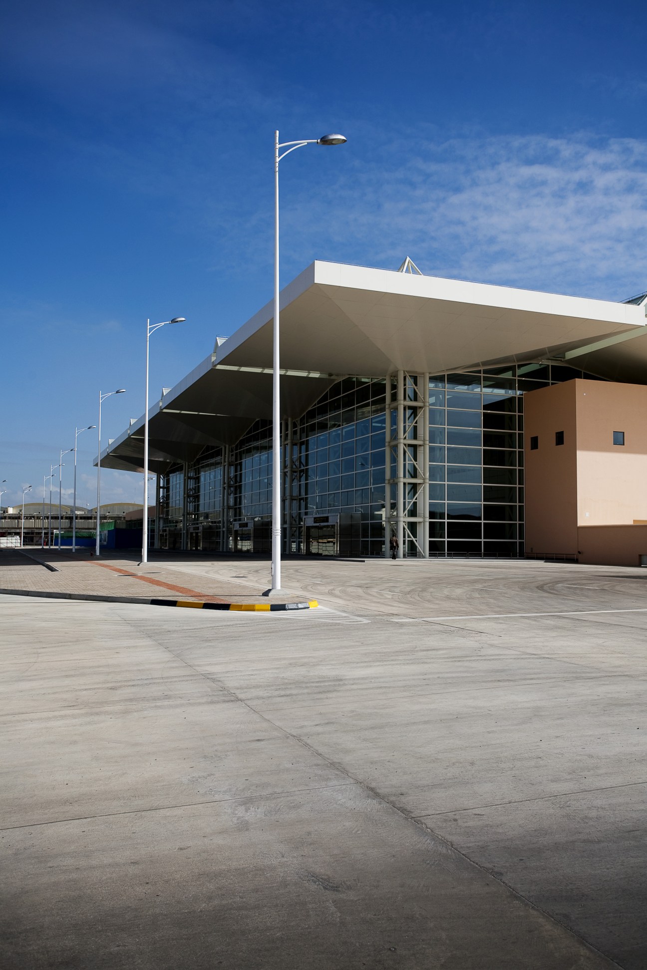 Modern airport terminal building with white canopy roof and glass facade under clear blue sky.