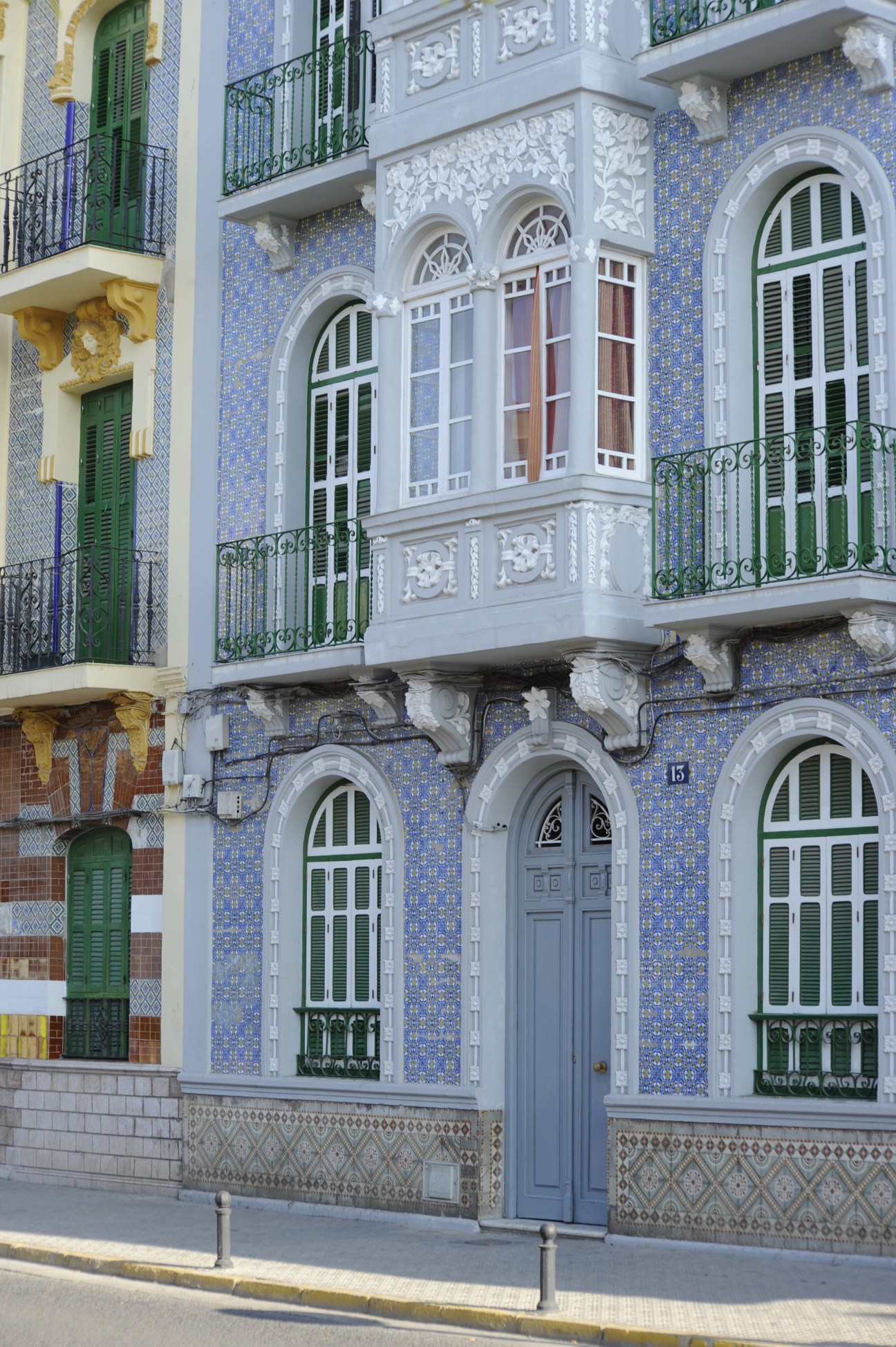 Ornate modernist building facade with blue tilework, white stone details, green shutters and wrought iron balconies.