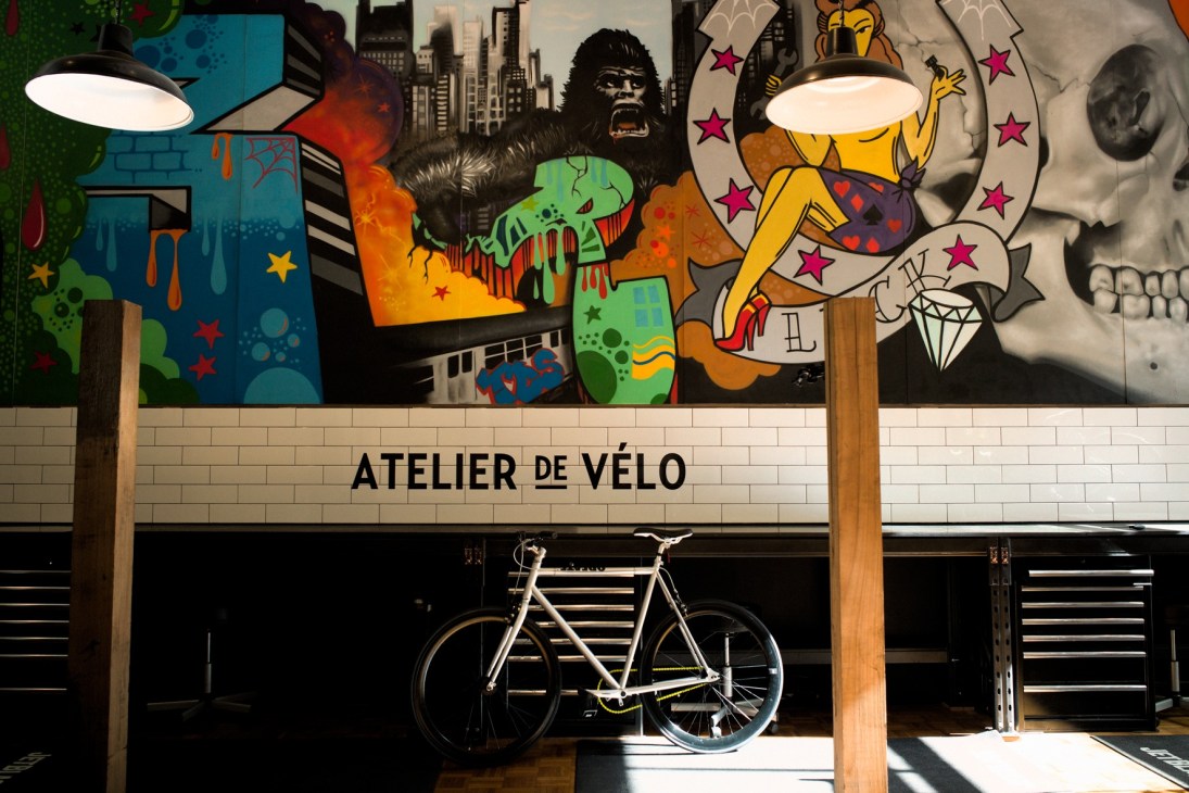Atelier de Vélo storefront with colorful graffiti mural and white bicycle displayed in window.