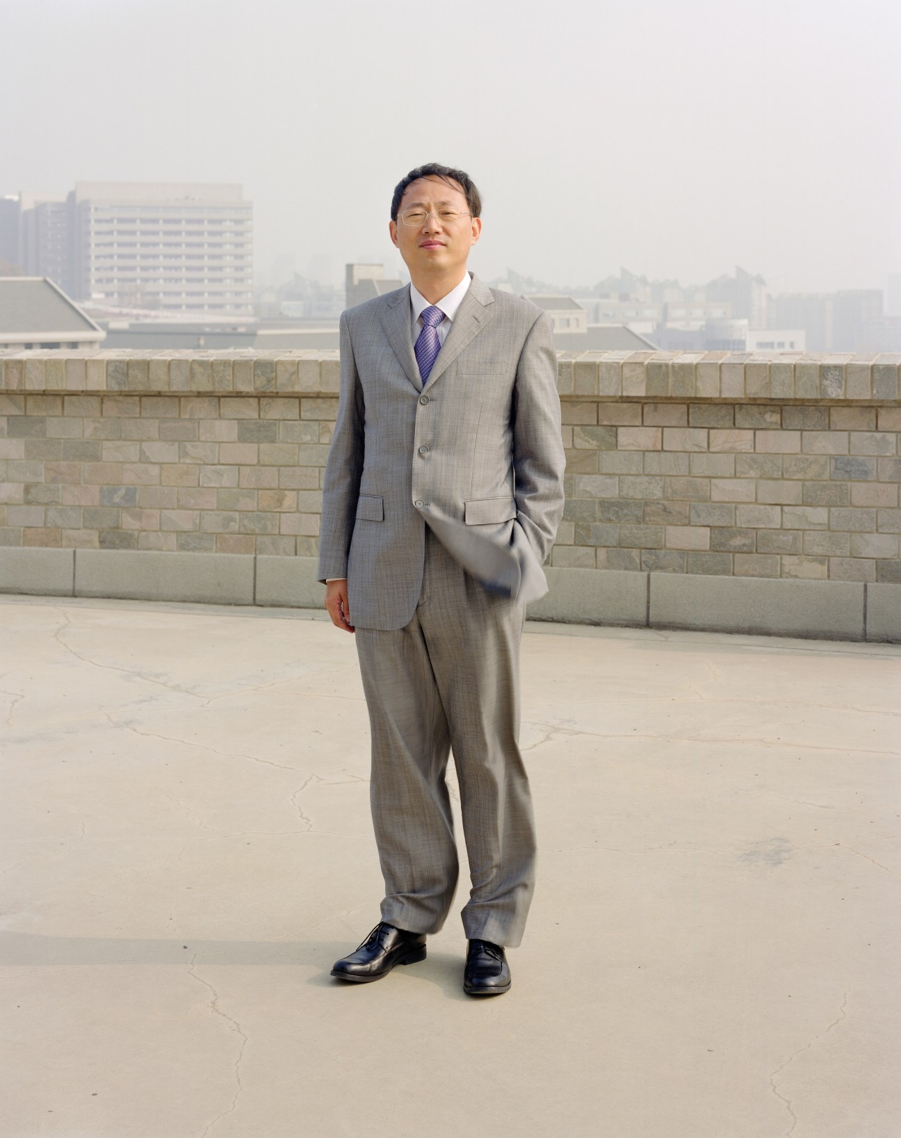 Yu Hengzhuang of Dalian Software Park stands on a rooftop in business attire overlooking the city skyline.