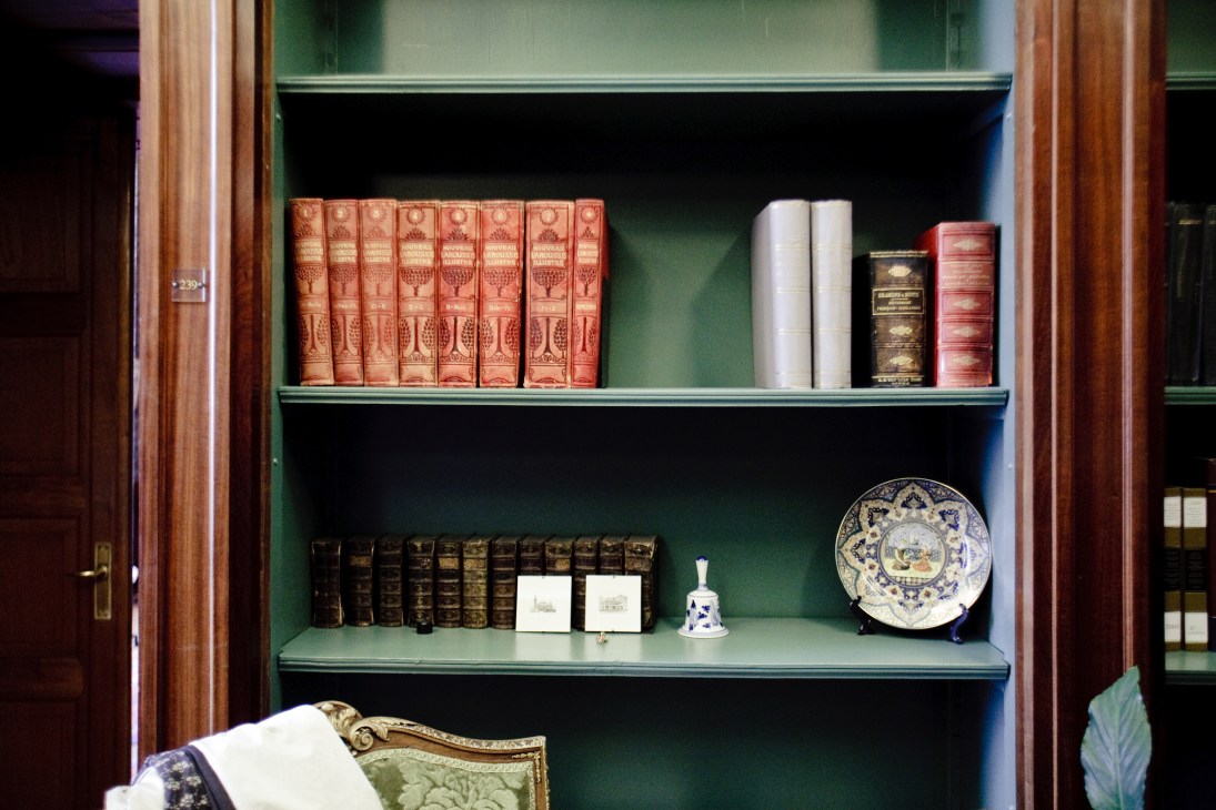 Green shelving displaying antique legal volumes and decorative objects including red leather-bound books and a blue and white porcelain plate.