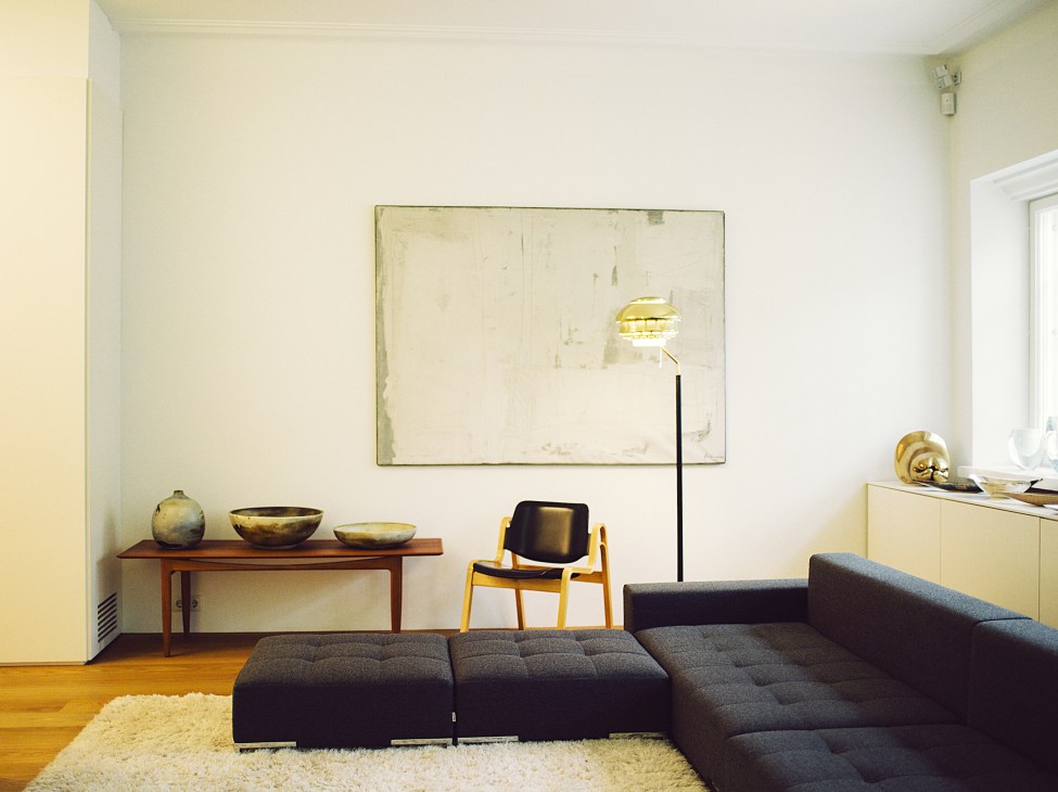 Modern living room with dark grey Alfa sofa, wooden table with brass bowls, yellow chair, and floor lamp.