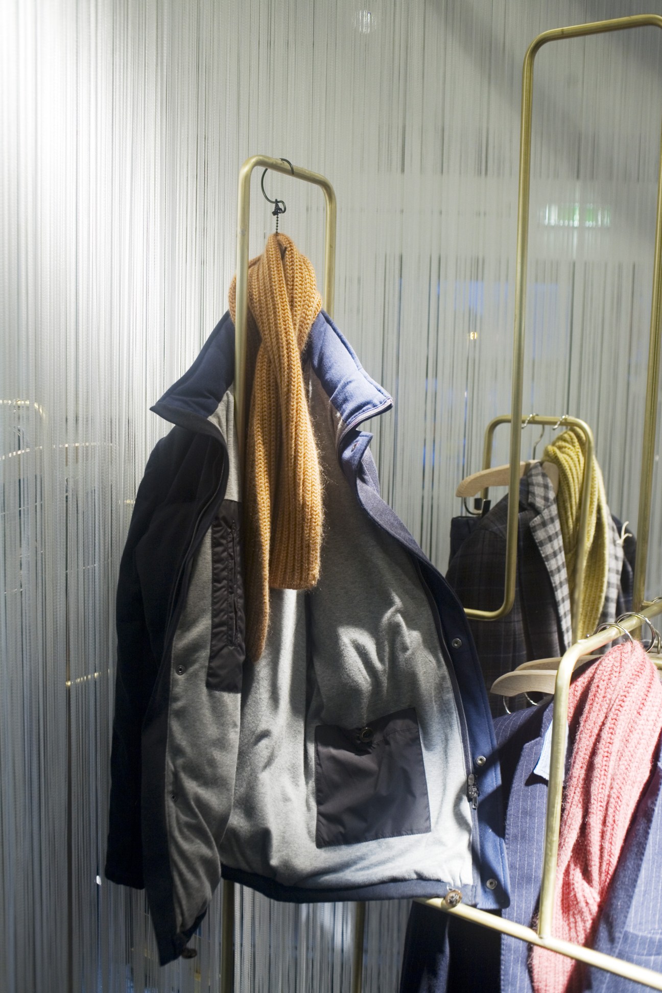 Boglioli sweatshirt material jacket with goose down lining displayed on a rack with a mustard scarf.