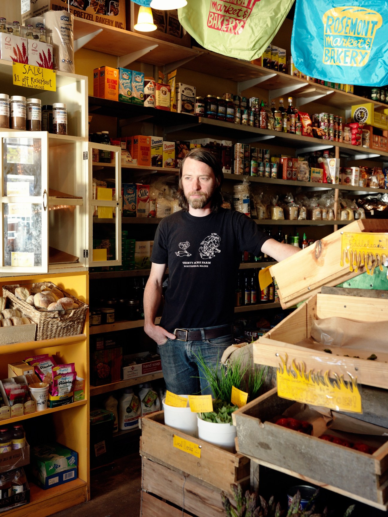 Man standing in Rosemont Market & Bakery with shelves of products and wooden produce boxes.