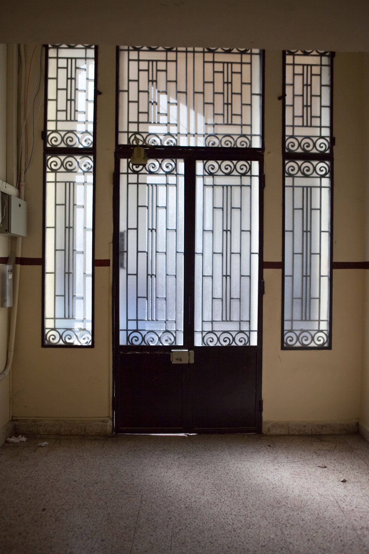 Art deco entrance doors with geometric patterned glass panels and ornamental metalwork in a Beirut apartment building lobby.