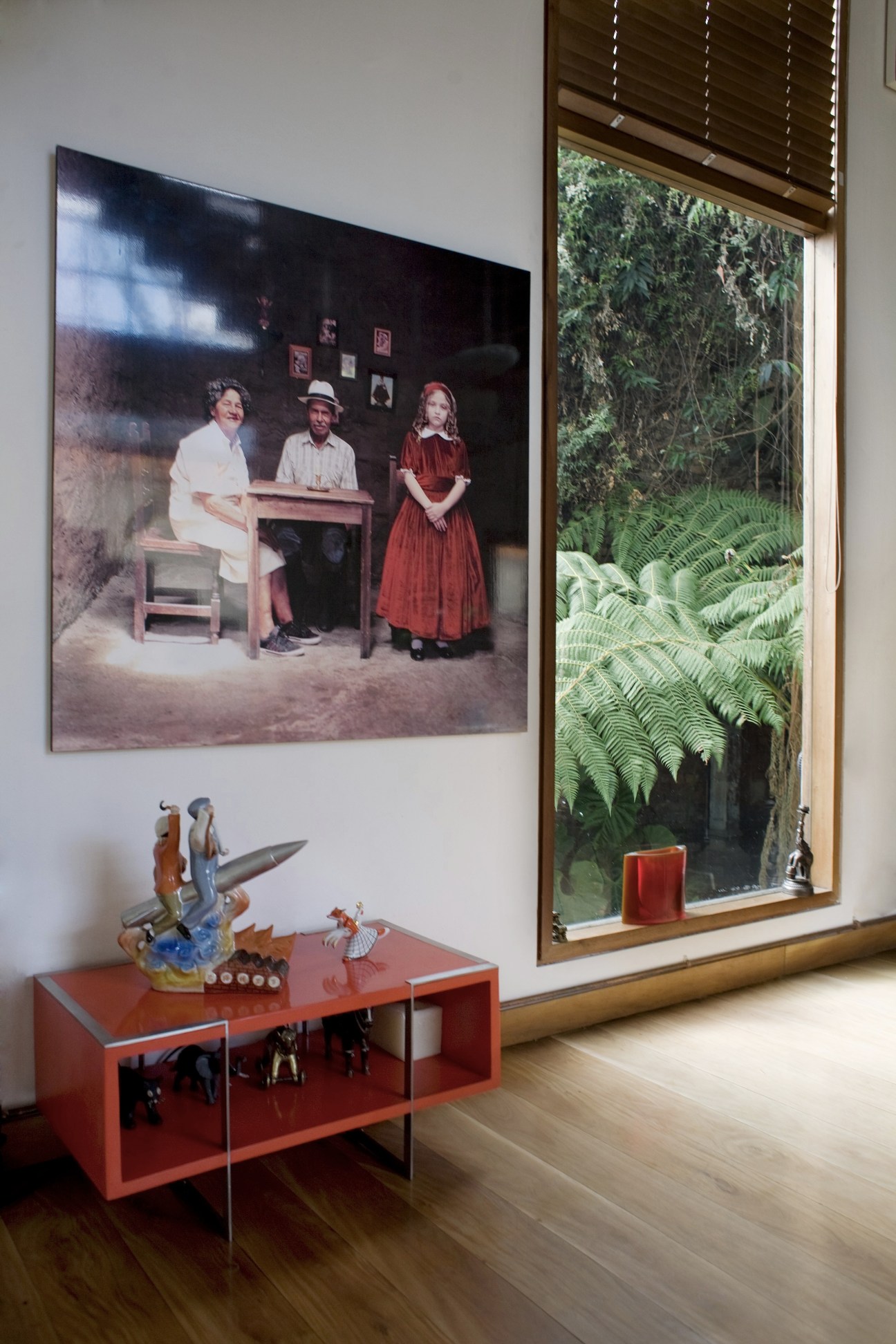 Interior room with red storage unit, decorative objects, and framed photograph on wall overlooking garden.