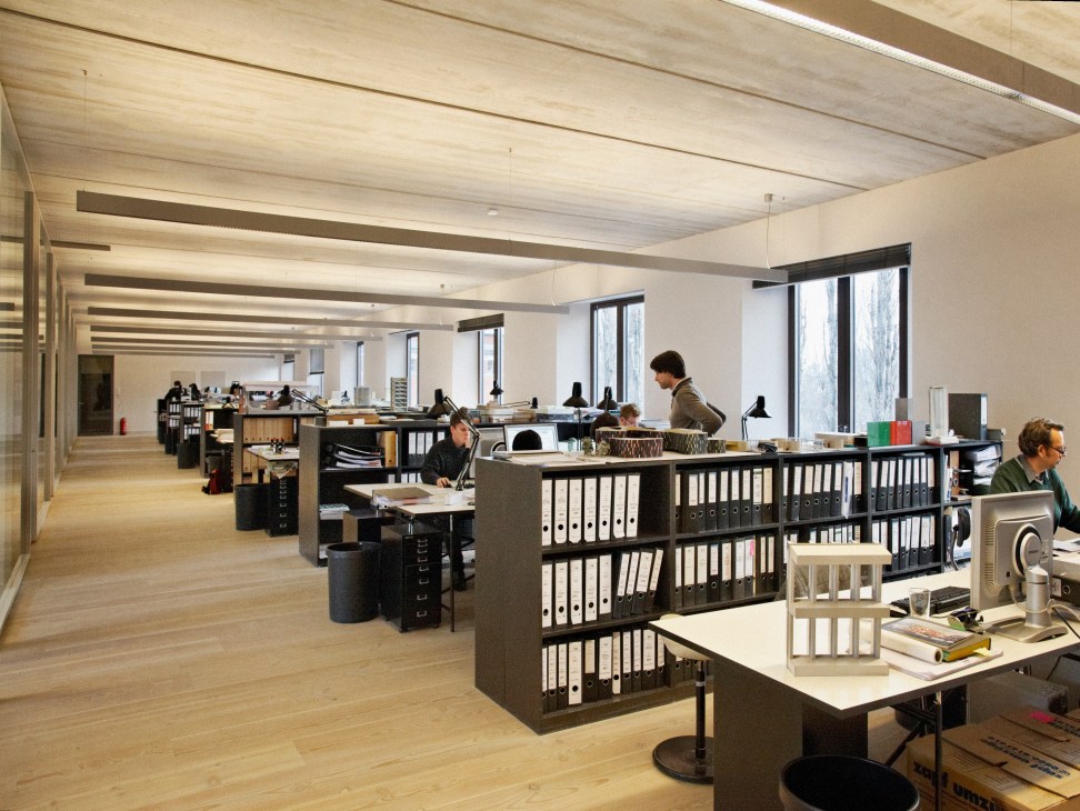 Open-plan design studio with wooden floors, black storage units, and large windows allowing natural light.