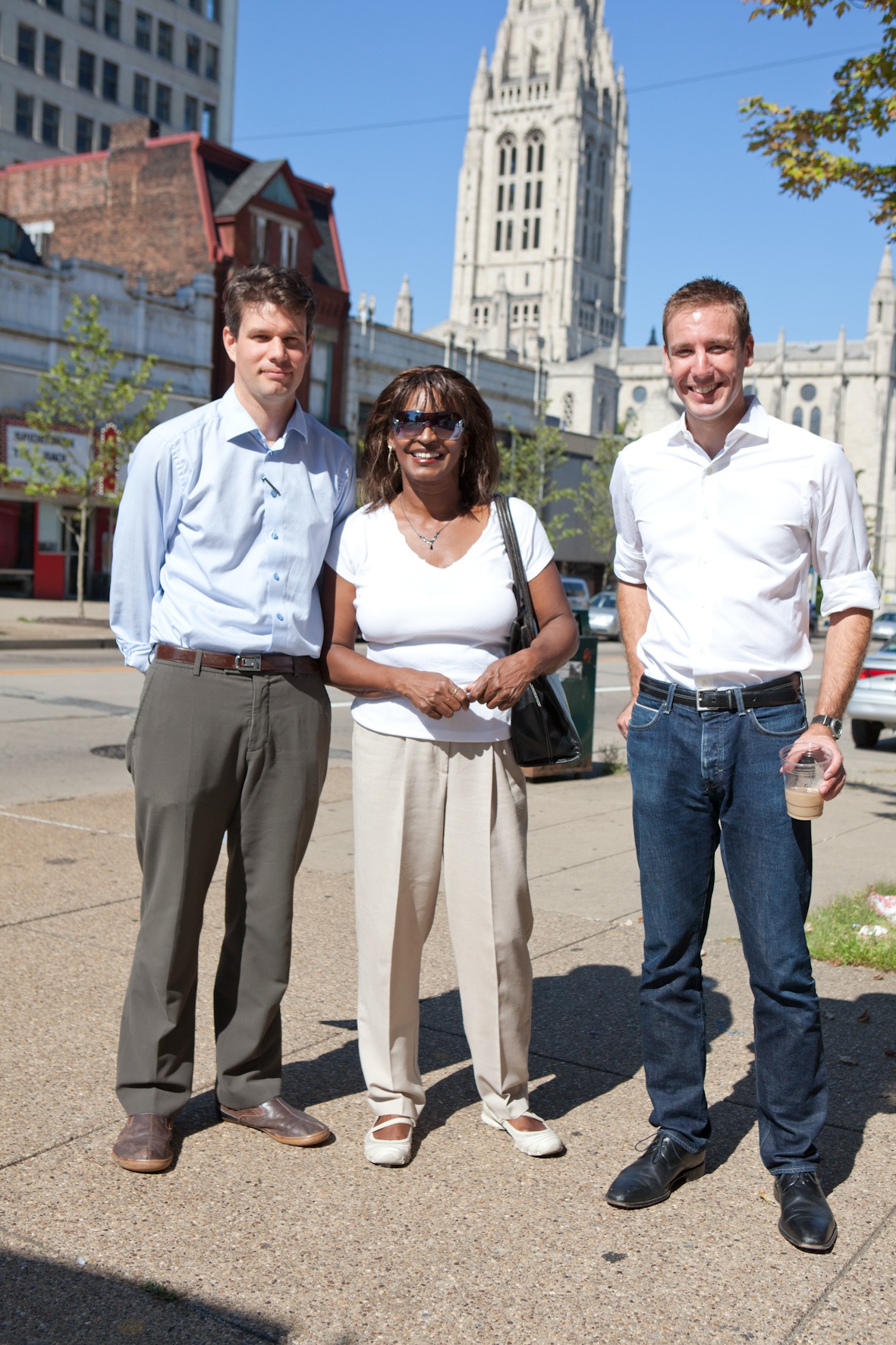 Three professionals stand on a Pittsburgh street with a Gothic cathedral visible in the background.