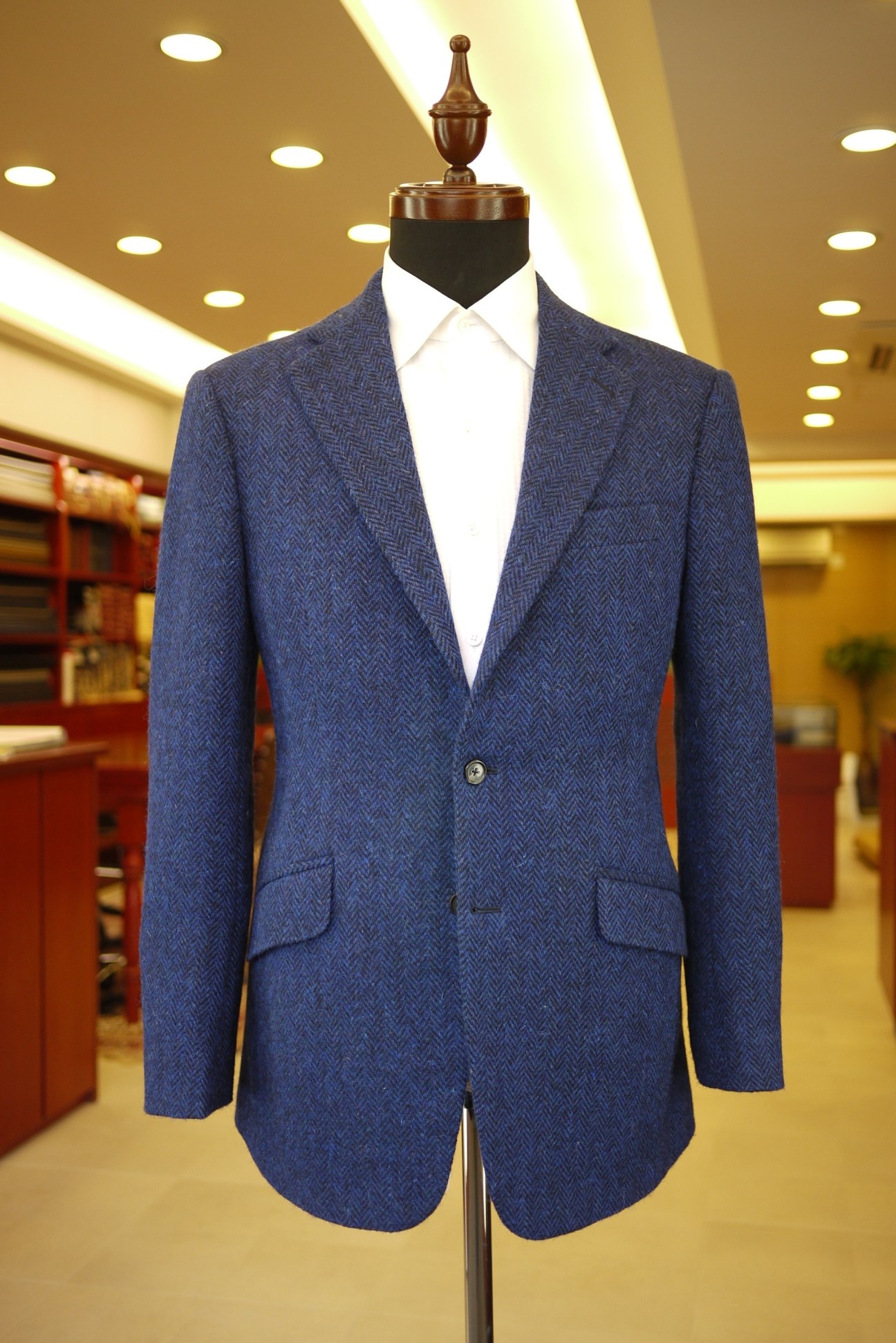Blue herringbone blazer displayed on a wooden dress form in a modern retail setting.