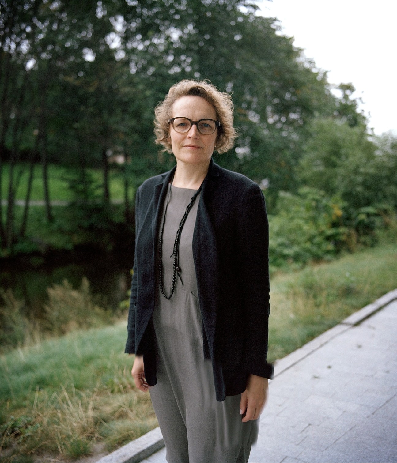Editor Gry Egenes stands outdoors wearing glasses and a dark cardigan over a grey dress.