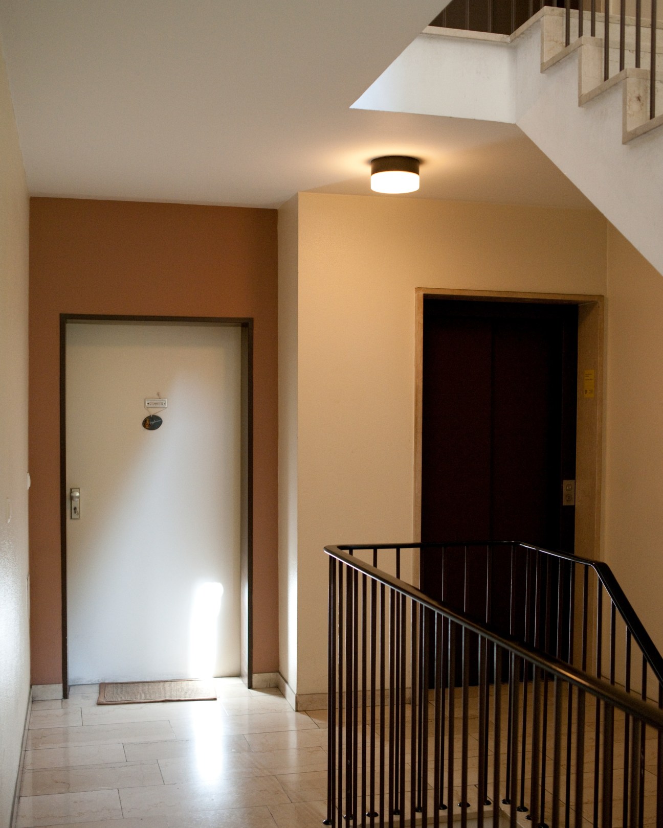 A sparse stairwell landing with tan walls, two doors, and a black metal railing.