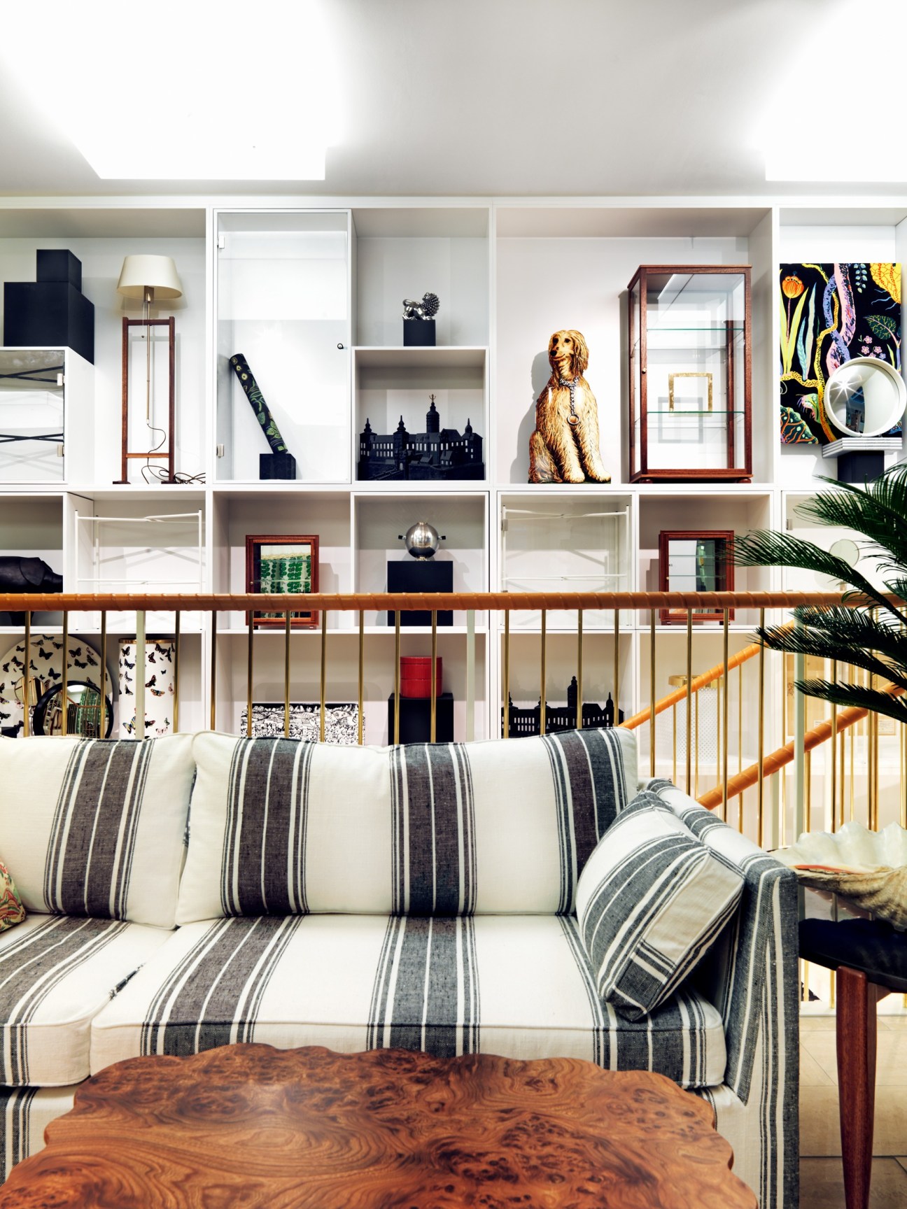 Living room display with striped sofa, wooden table, and shelving unit filled with decorative objects at Svenskt Tenn store.