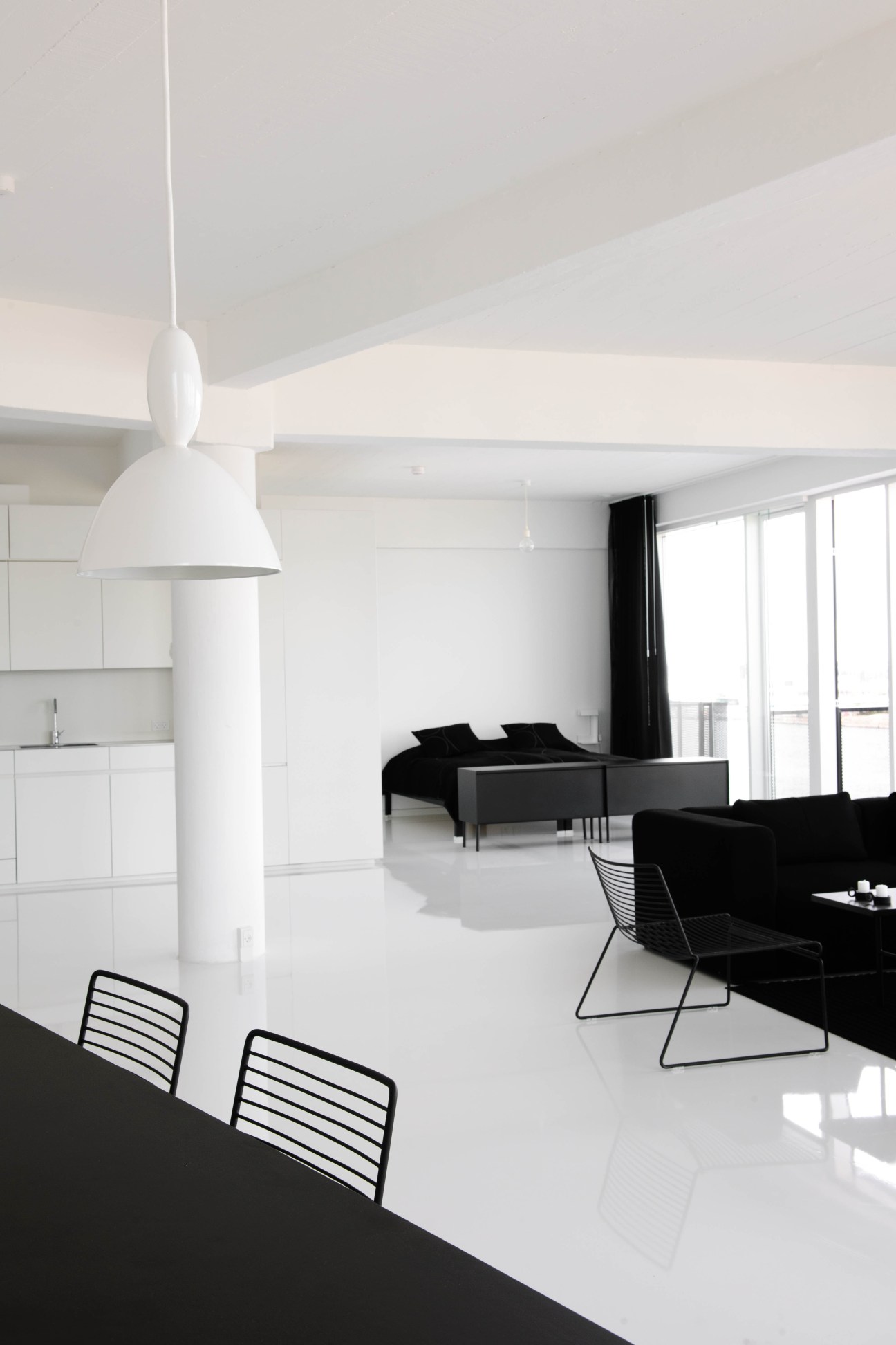 Minimalist apartment interior at Stay Hotel Copenhagen with white pendant lamp, black furniture, and open-plan layout.