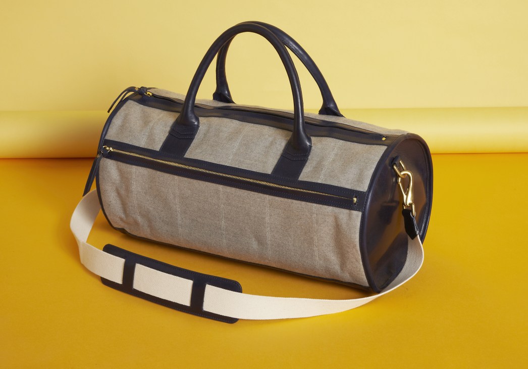 Libero Ferrero canvas and leather duffel bag with navy handles and shoulder strap on yellow background.