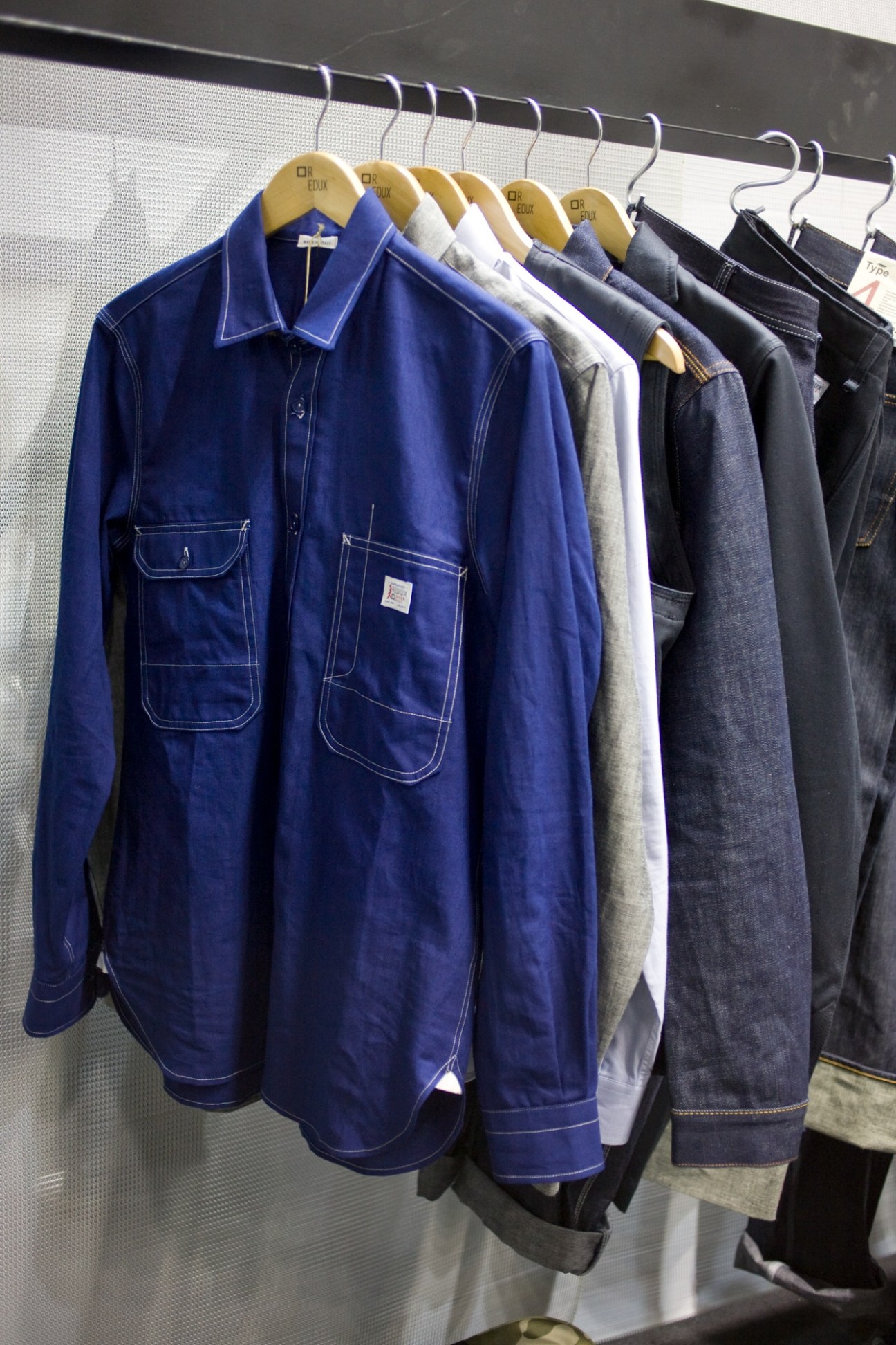 Redux denimwear collection displayed on wooden hangers showing various denim shirts and jackets in blue, white and black.