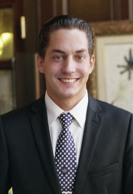 Professional headshot of a man in a dark suit and patterned tie smiling at the camera.