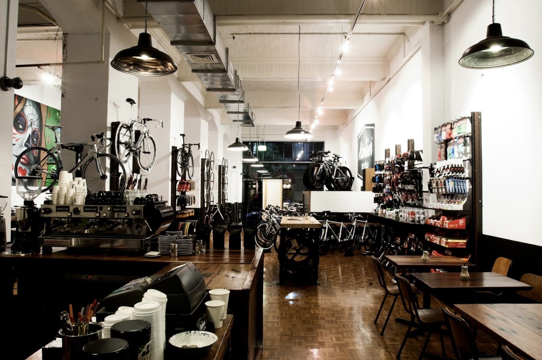 Interior of Atelier de Vélo showing bicycles on display, espresso machines, and retail space with pendant lighting.