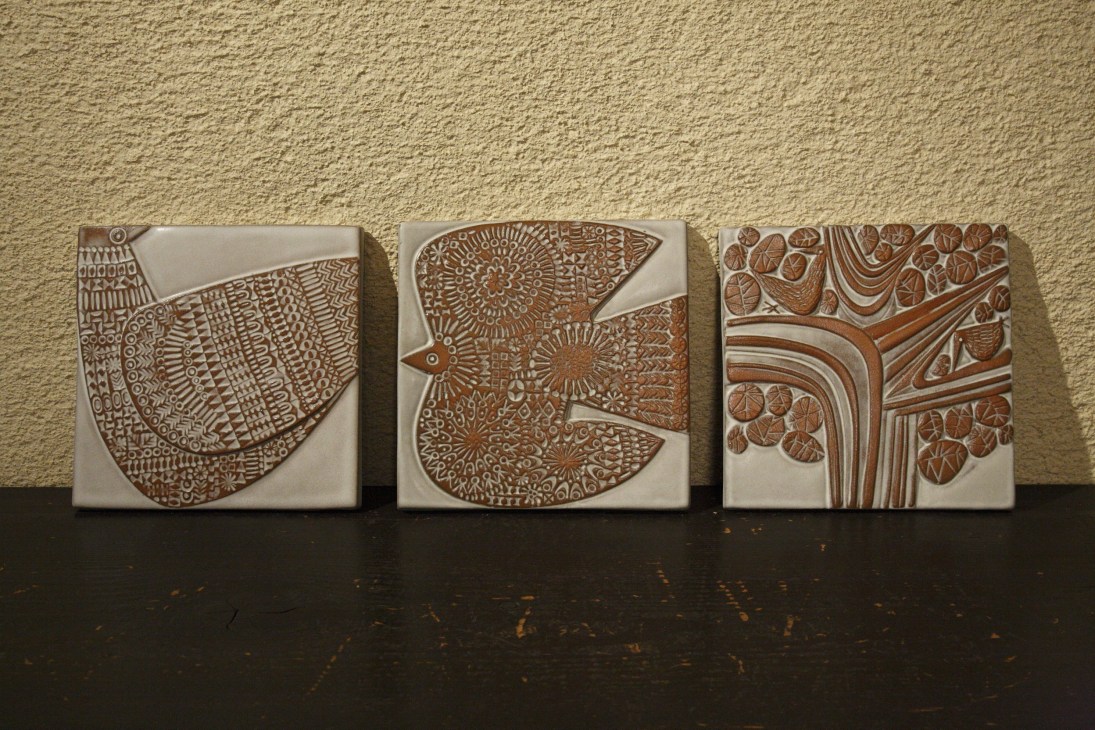 Three ceramic tiles with intricate brown bird and nature-inspired relief designs on cream backgrounds.