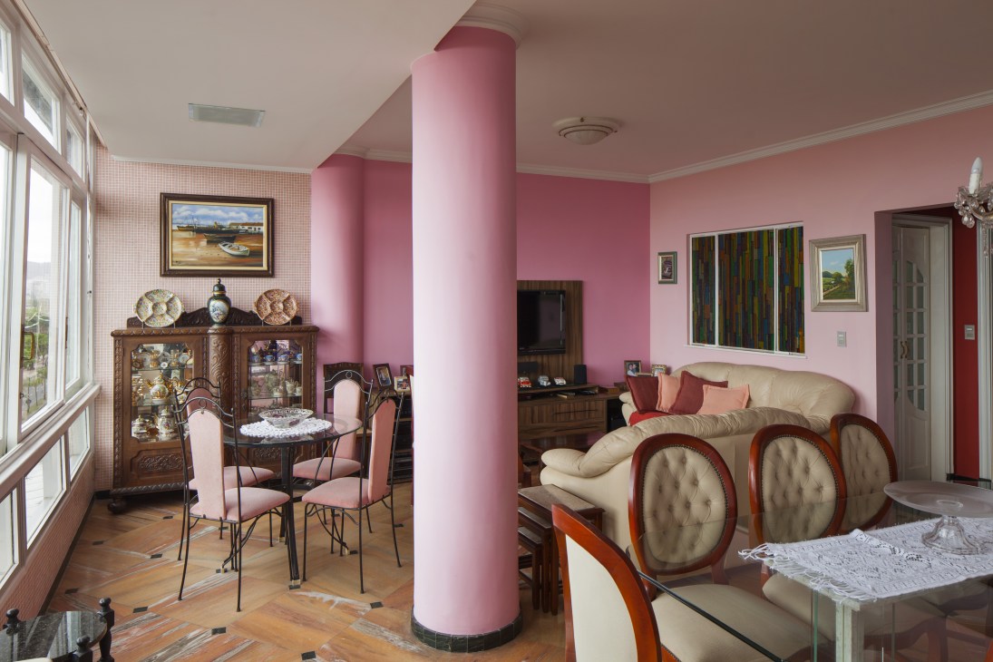 Interior of a combined apartment with pink walls, supporting columns, wooden furniture and large windows overlooking the beach.