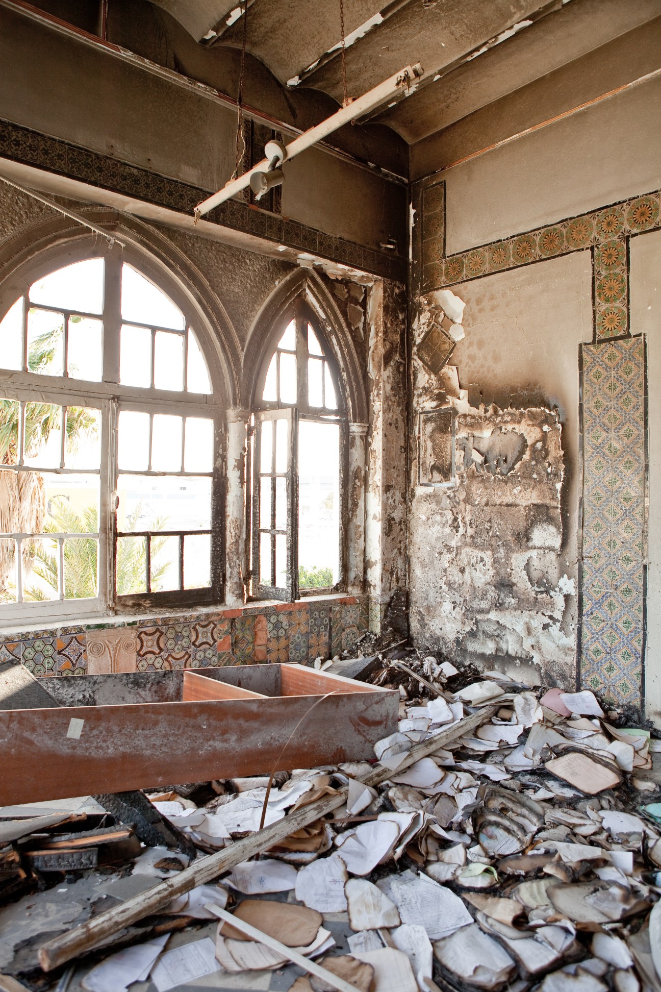 Ransacked police station interior with scattered debris, deteriorating walls, decorative tilework, and arched windows in La Goulette.