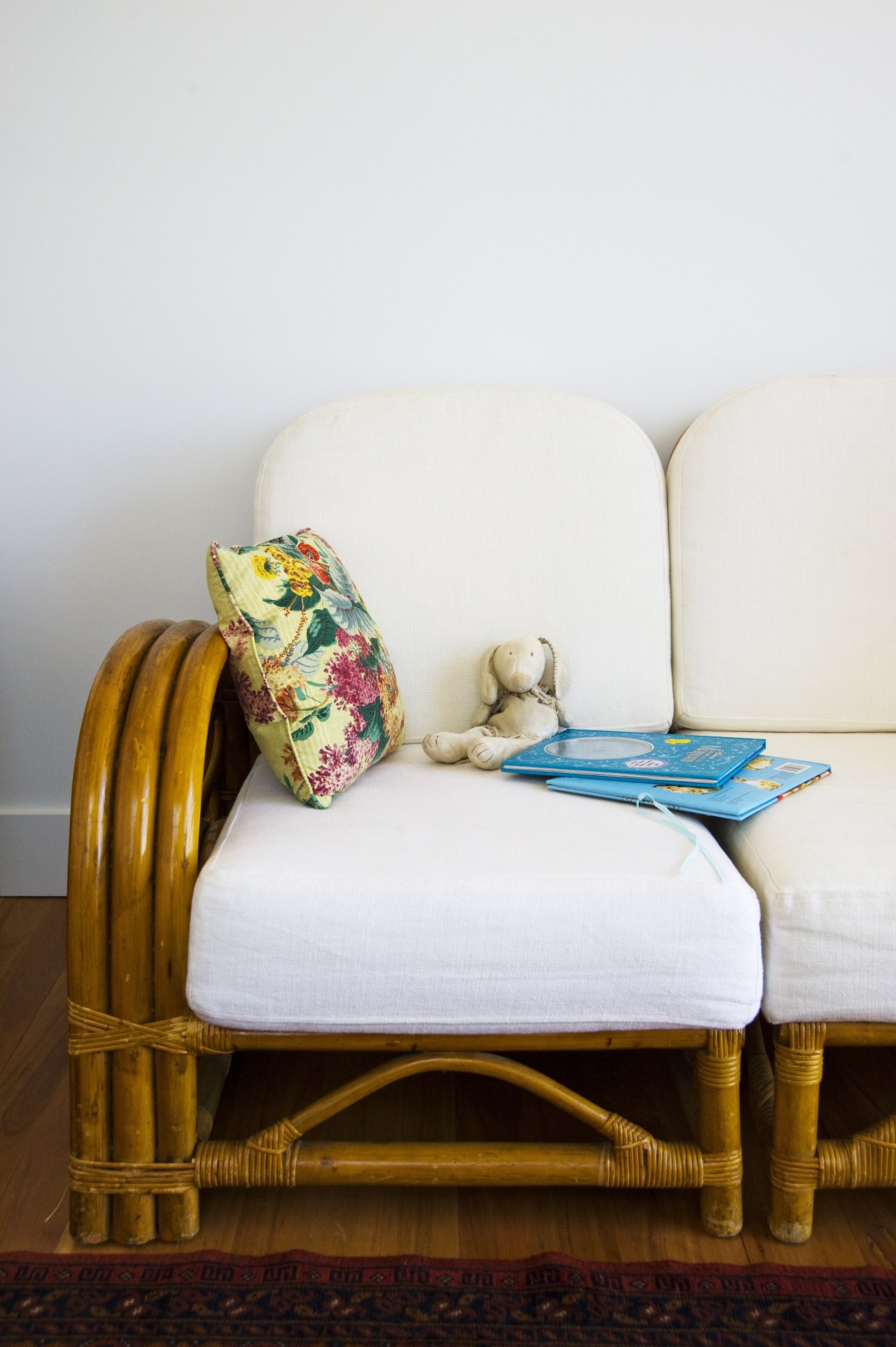 A child's bedroom with a wooden day bed, white cushions, floral pillow, stuffed rabbit, and blue books.