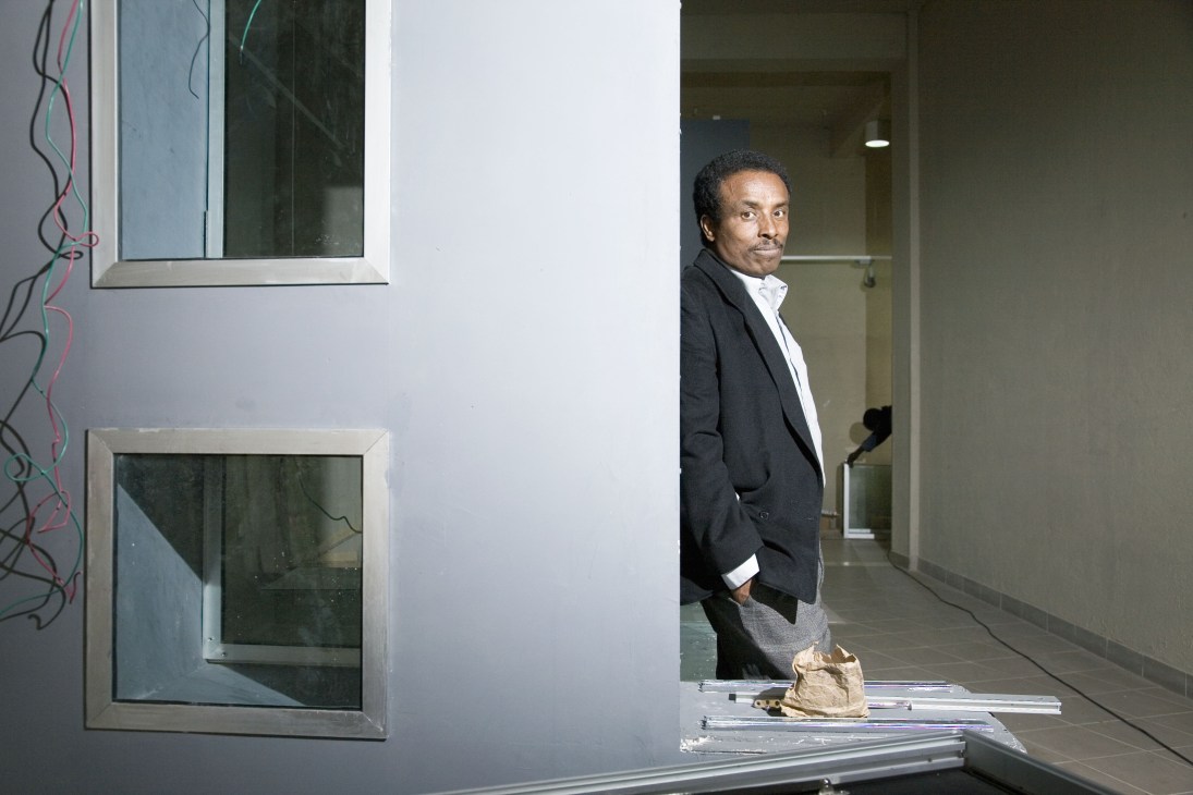 Architect Fasil Giorghis stands in a modern hallway beside a minimalist white wall with windows and wiring.