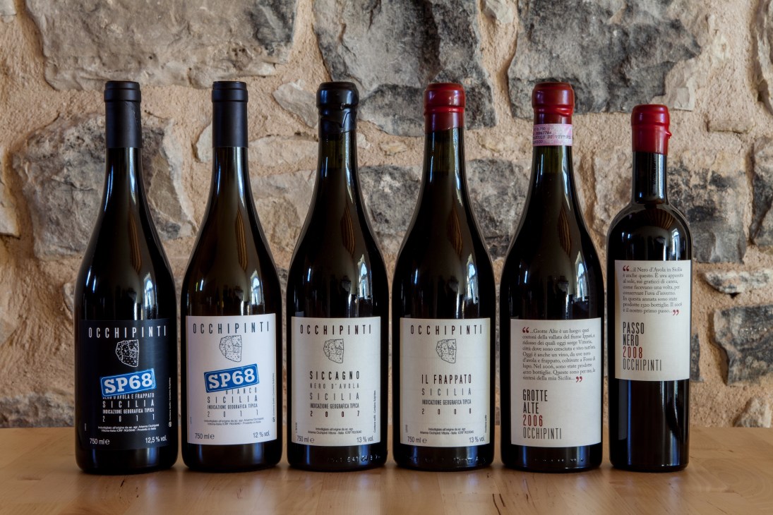 Six bottles of Arianna Occhipinti wine displayed against a rustic stone wall.