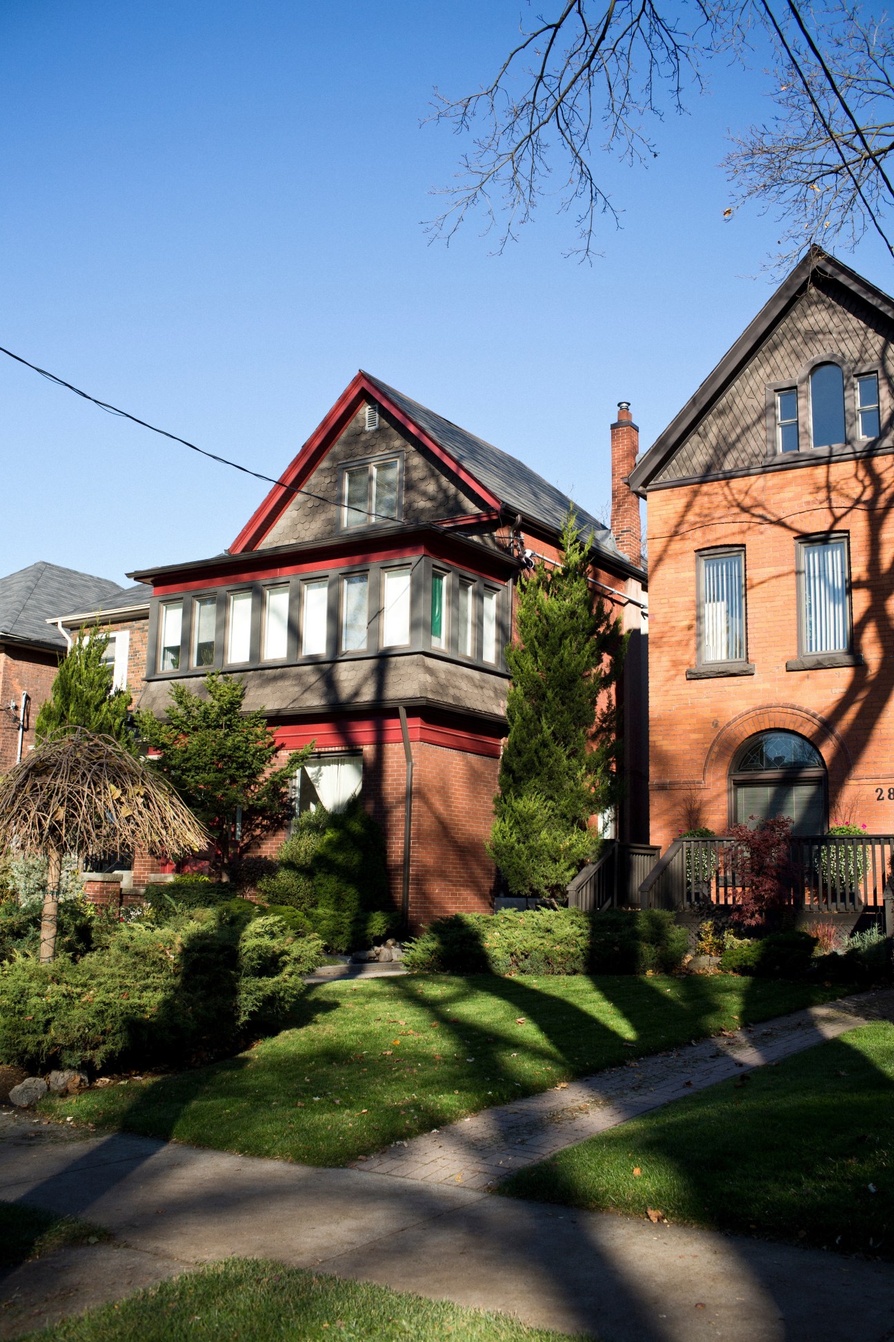 Victorian and Edwardian redbrick houses with manicured gardens on a tree-lined street in Toronto's Junction neighbourhood.