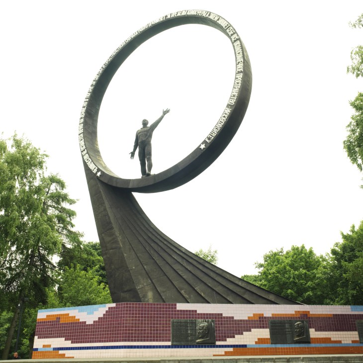 Soviet monument to astronauts in Kaliningrad featuring a large curved metal structure with a figure inside a circular ring
