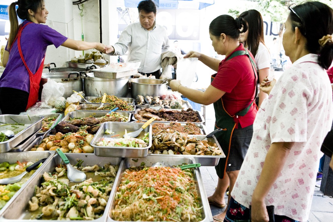 Vendors serve Thai food from metal trays at a busy street market stall in Bangkok's Ari neighbourhood.