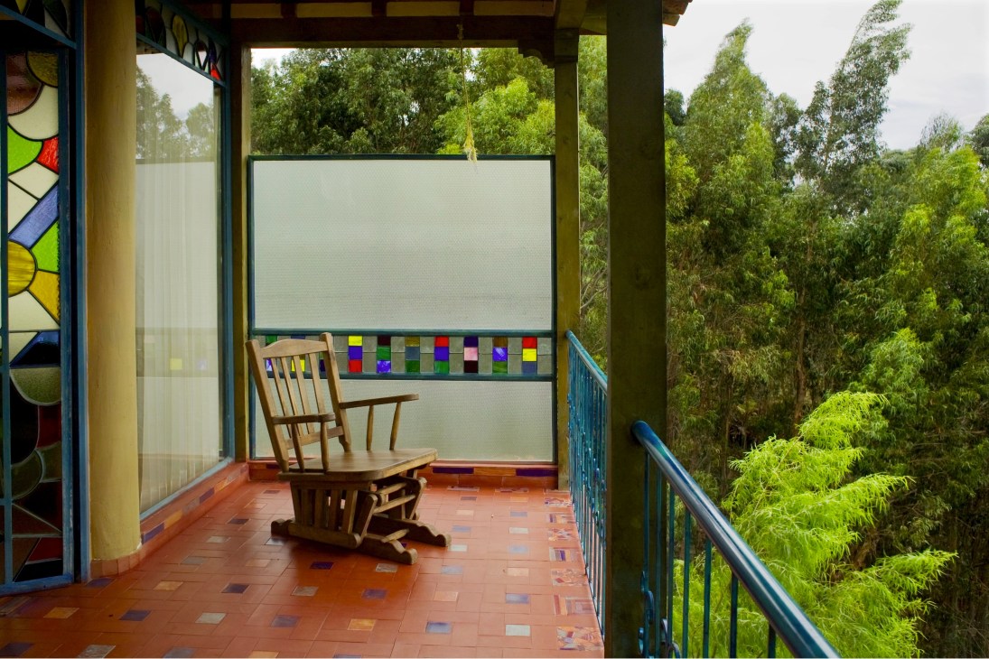 Covered balcony with wooden rocking chair overlooking lush green forest and hills.