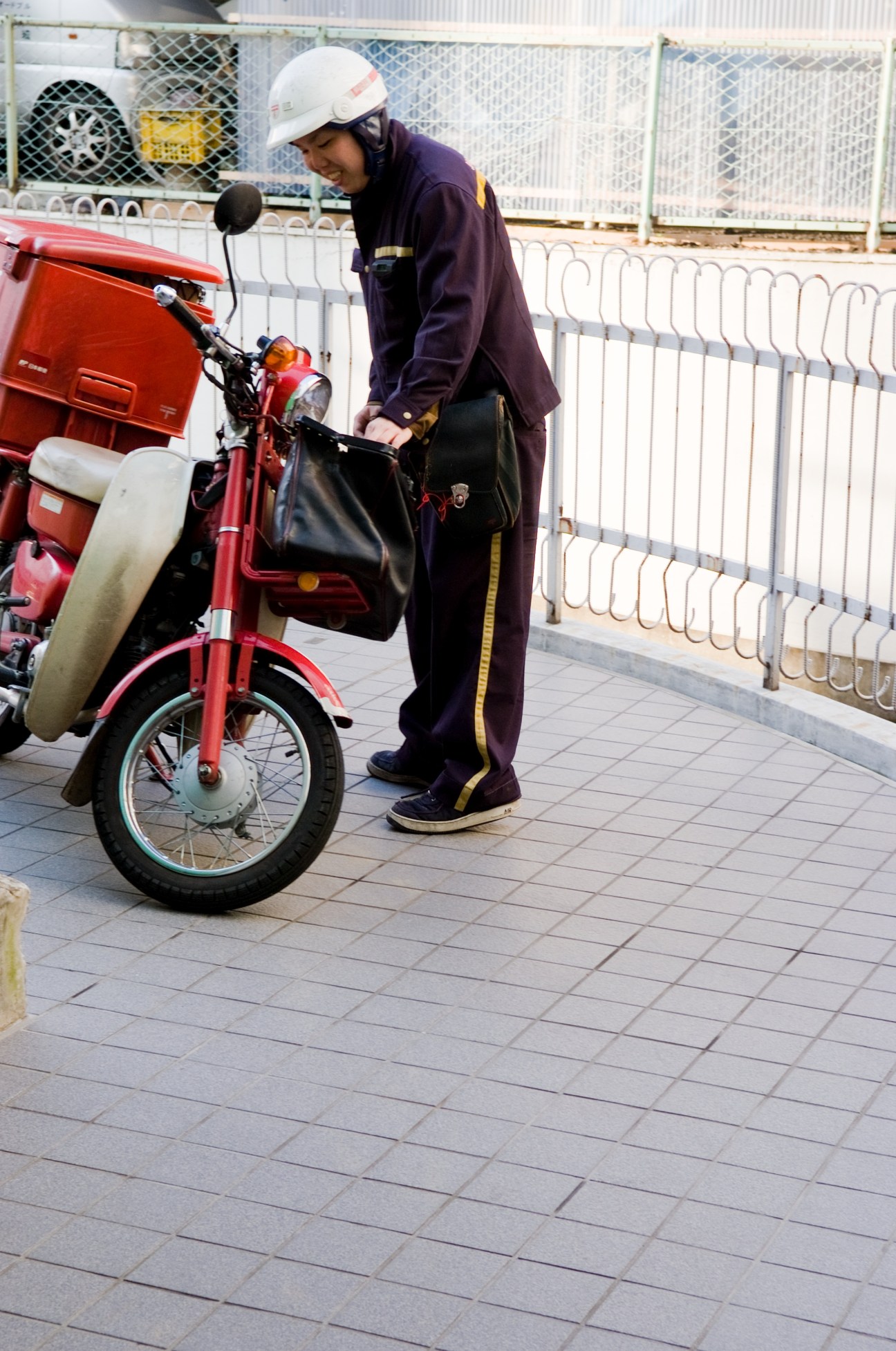 Postman in uniform and white helmet standing with a red Honda Super Cub scooter.