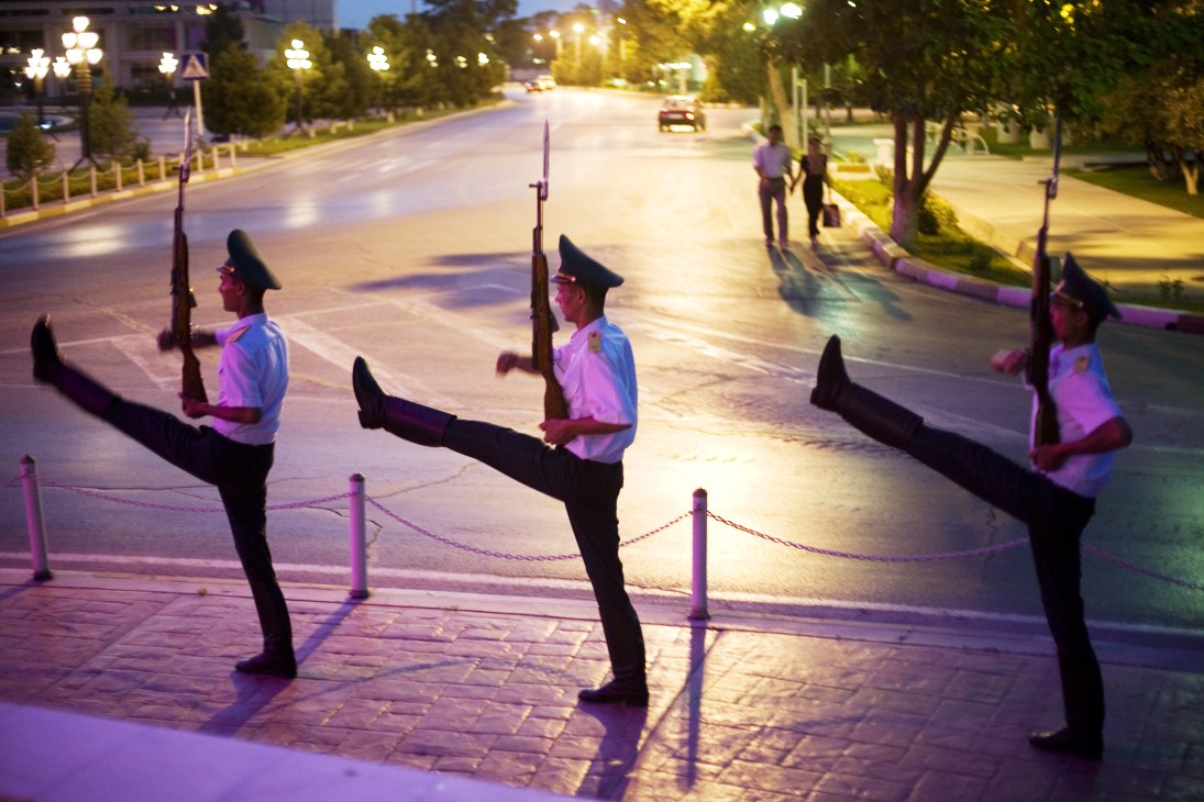 Soldiers marching in formation with rifles under the Arch of Neutrality in Ashgabat's central square at dusk.