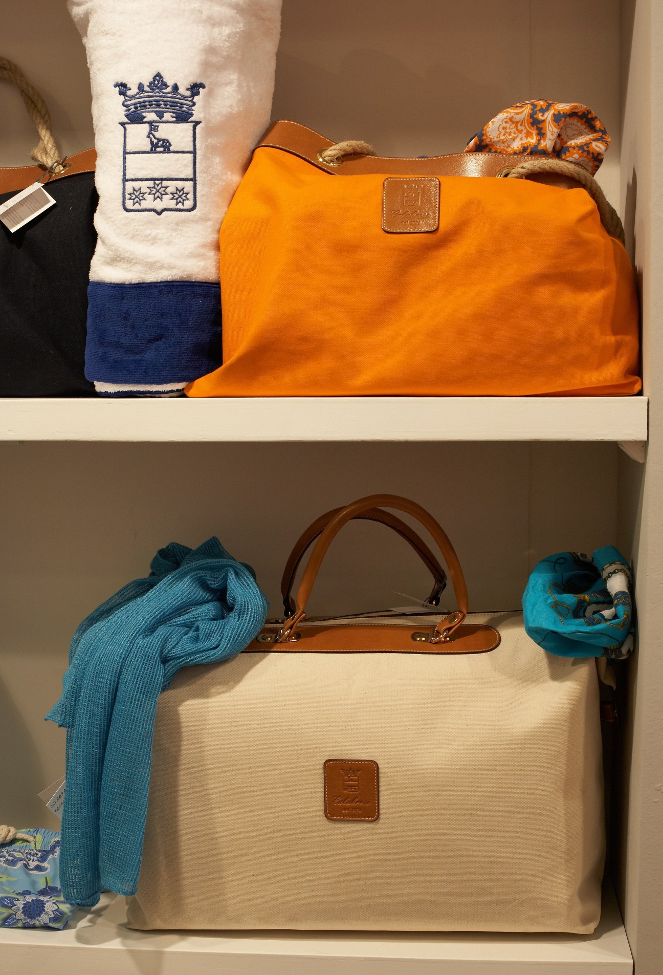 Calabrese bags and beach towel displayed on shelves, featuring orange and cream canvas bags with leather handles and blue textiles.