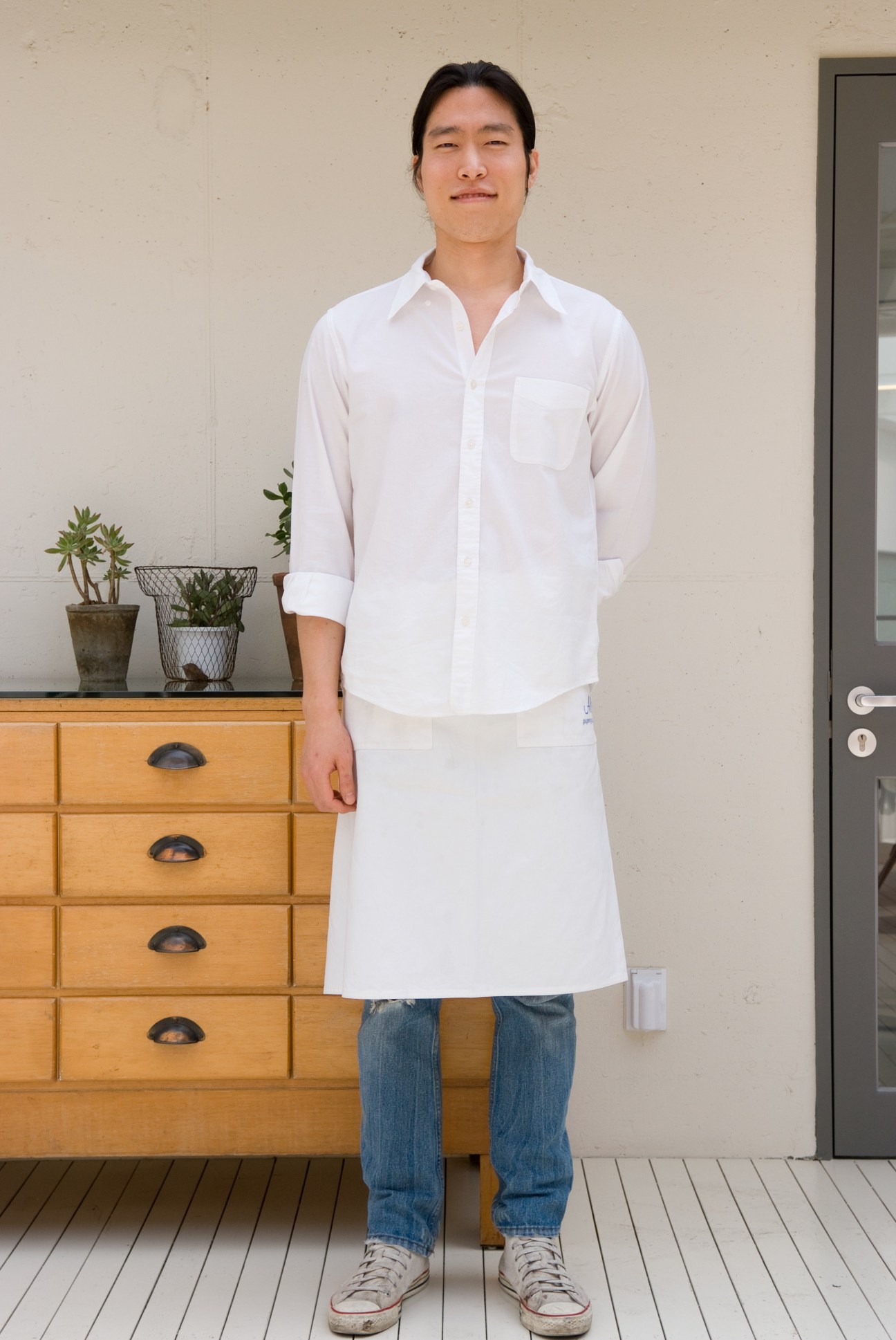 Oh Hwang-ryul, a waiter, stands in a minimalist interior wearing a white shirt and blue jeans.