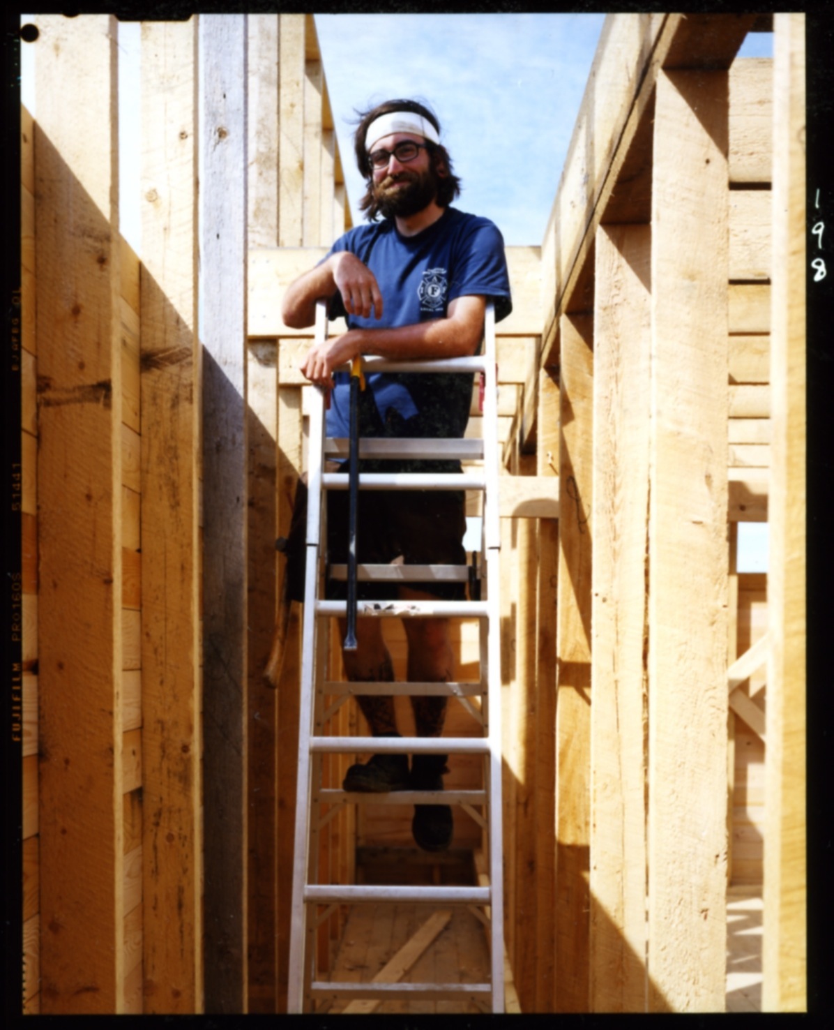 Man on ladder during construction wearing headband and blue t-shirt