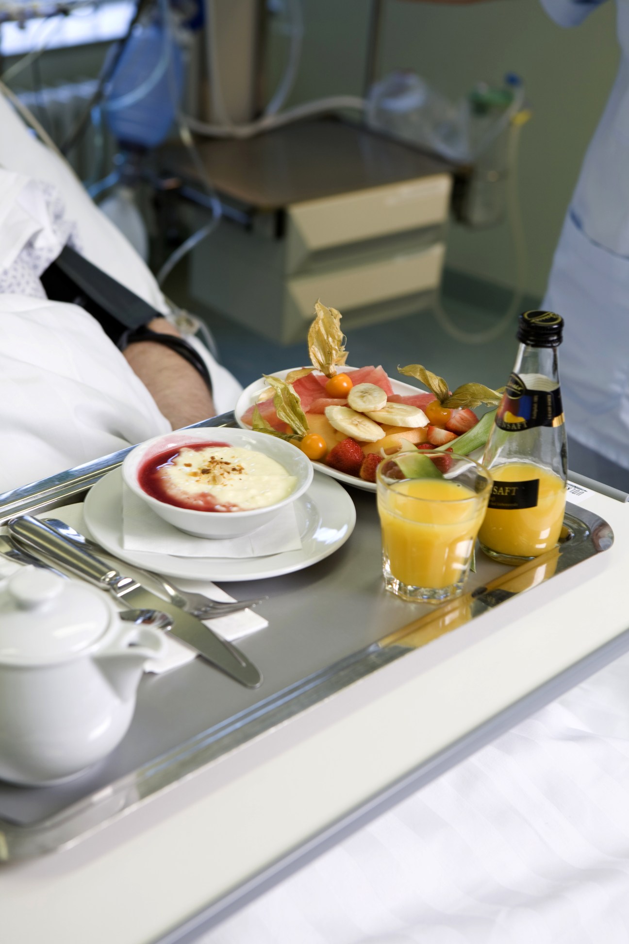 A hospital meal tray with soup, fresh fruit, juice, and utensils served to a patient.