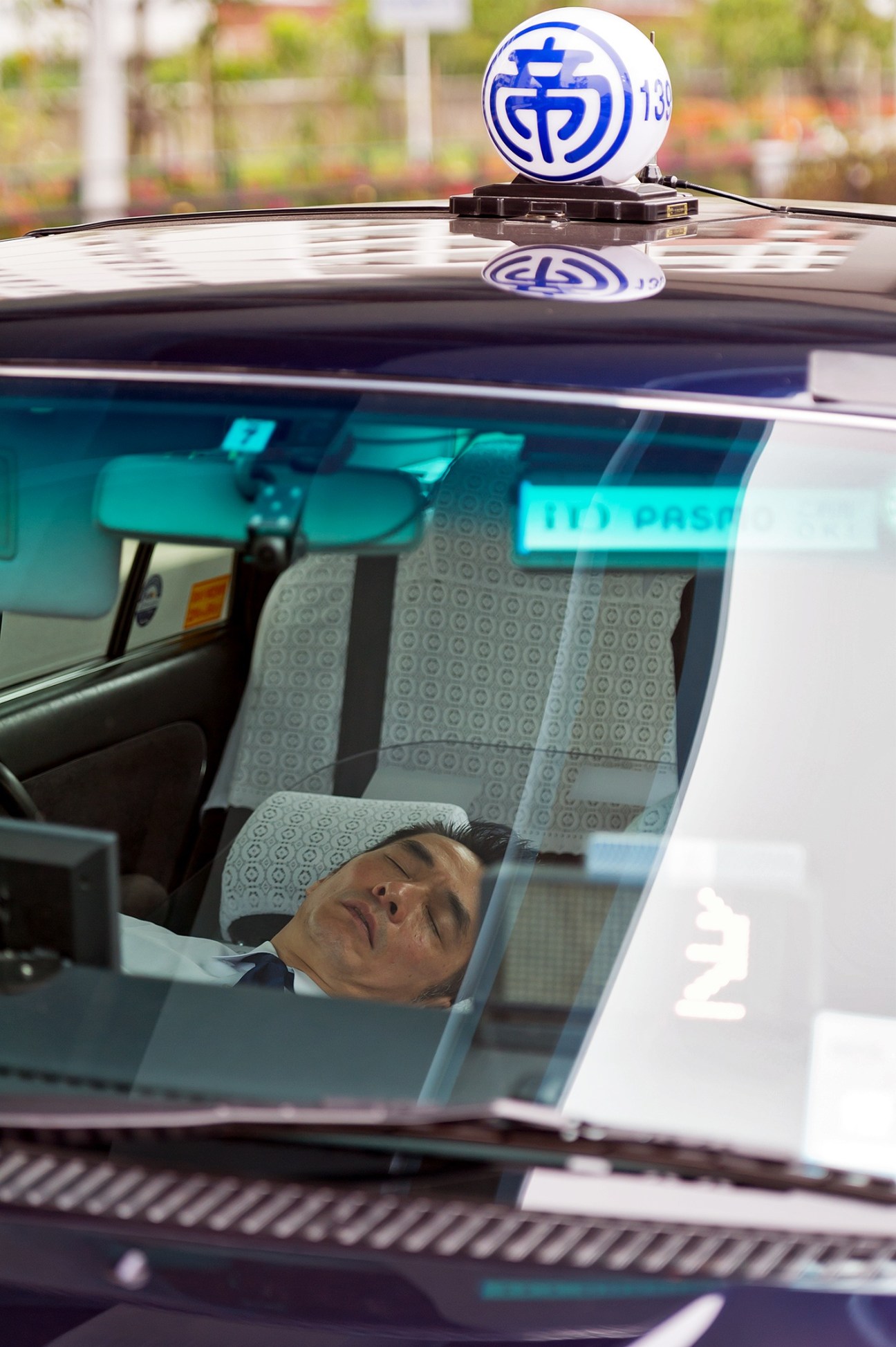 Tokyo taxi driver sleeping inside a Nihon Kotsu taxi with the company's blue and white logo visible on the roof.