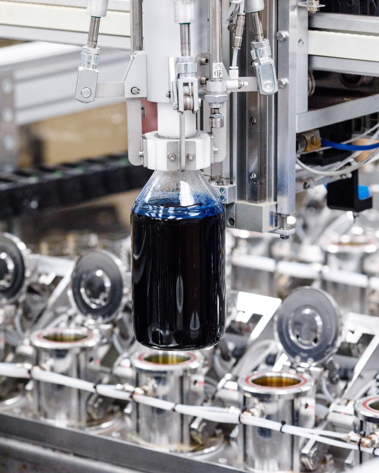 Laboratory apparatus dispensing dark blue dye into a glass bottle suspended above containers of liquid.