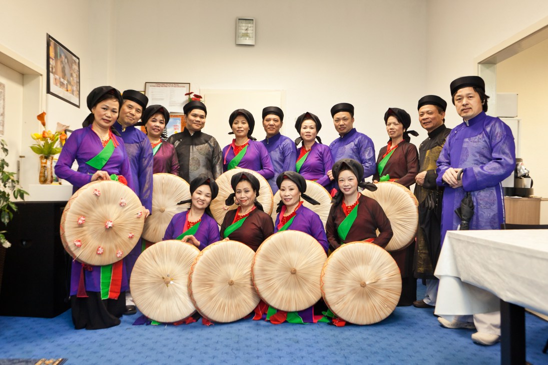 Vietnamese folk music group in traditional áo dài clothing holding conical hats at Dong Xuan Center in Berlin.