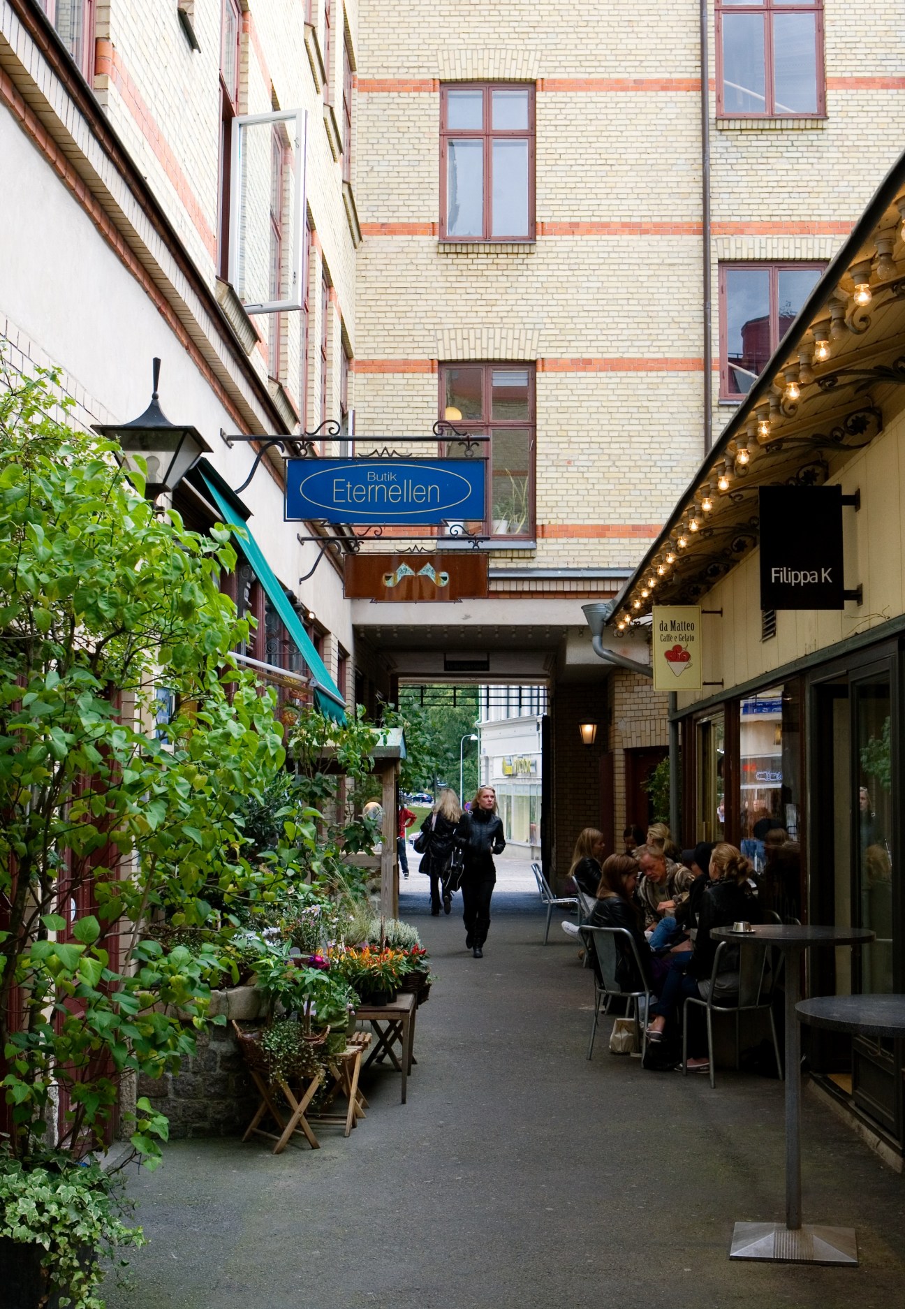 Pedestrians walk through a charming cobblestone shopping street in central Gothenburg lined with brick buildings and storefronts.