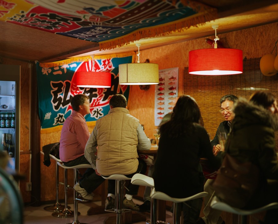 Interior of Ezo Seafood restaurant with customers seated at counter under red and yellow pendant lights.