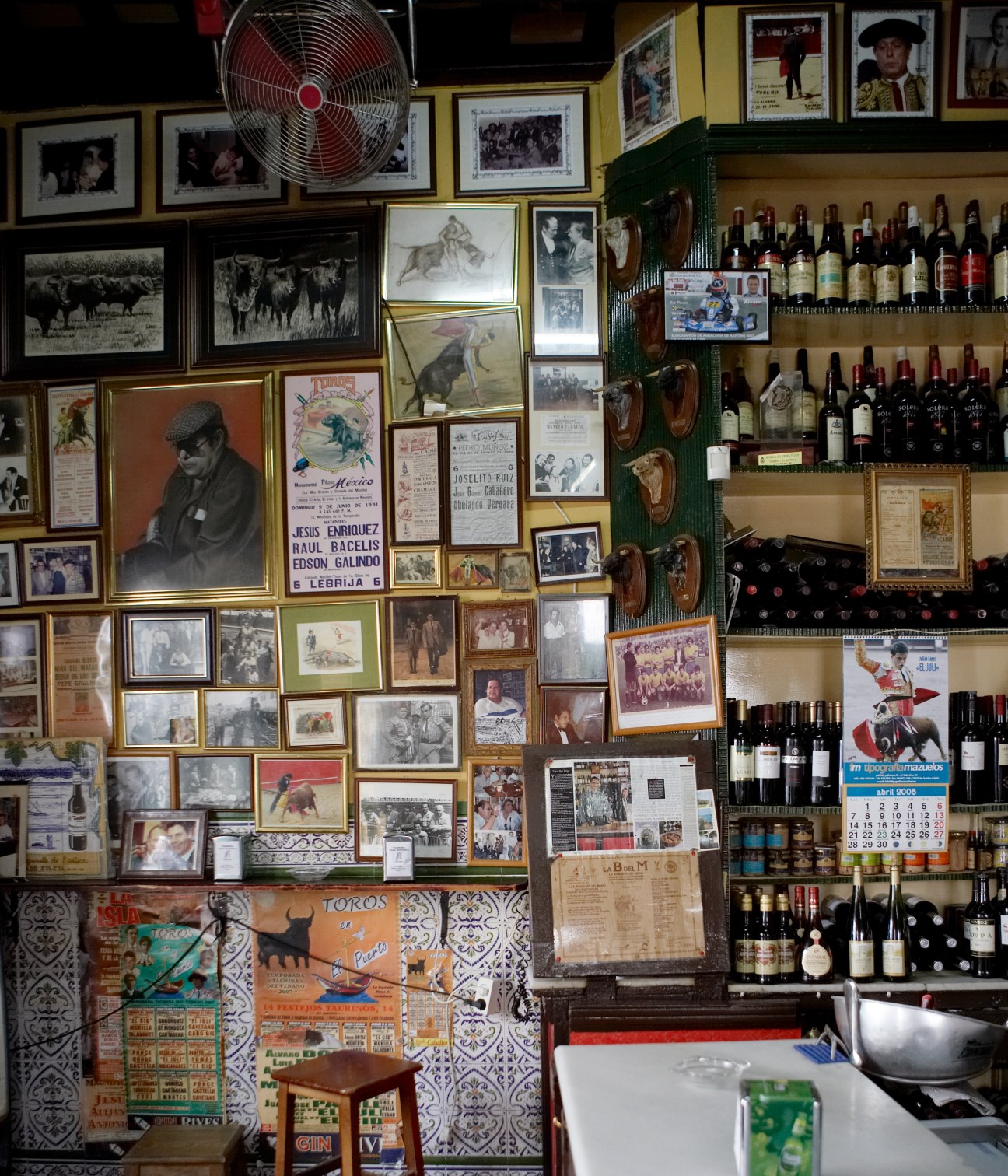 Interior of Casa Manteca bar with framed bullfighting photos, paintings, and wine bottles on shelves.