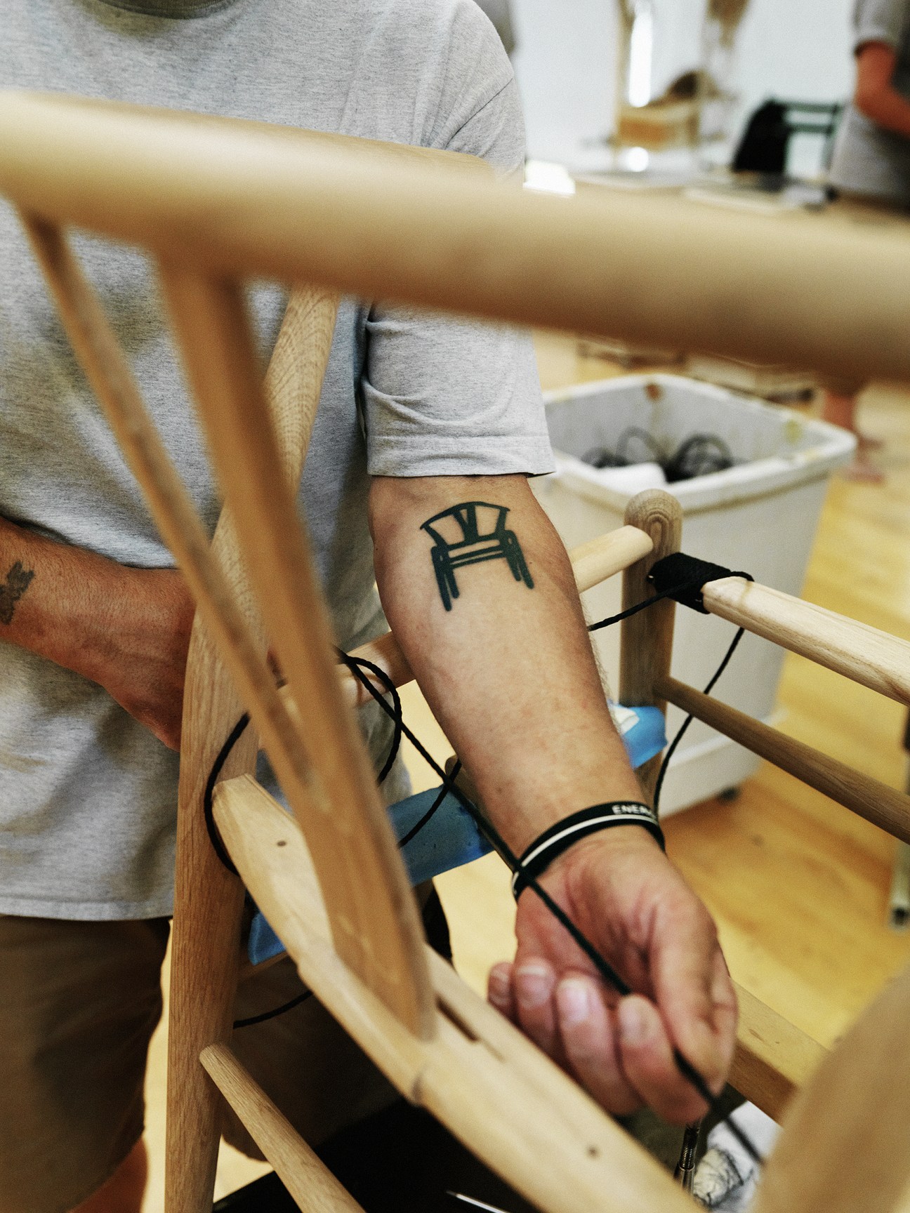 Factory worker with chair tattoo assembles wooden furniture components on the production floor.