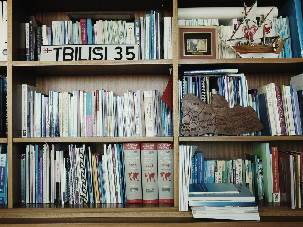 Wooden shelving unit filled with books, reference materials, and decorative objects including a wooden ship model and map.