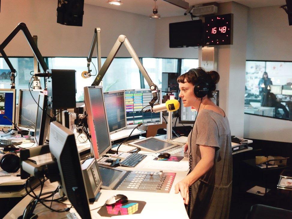 FM4 host Esther Csapo wearing headphones at a radio studio desk with microphone and broadcasting equipment.