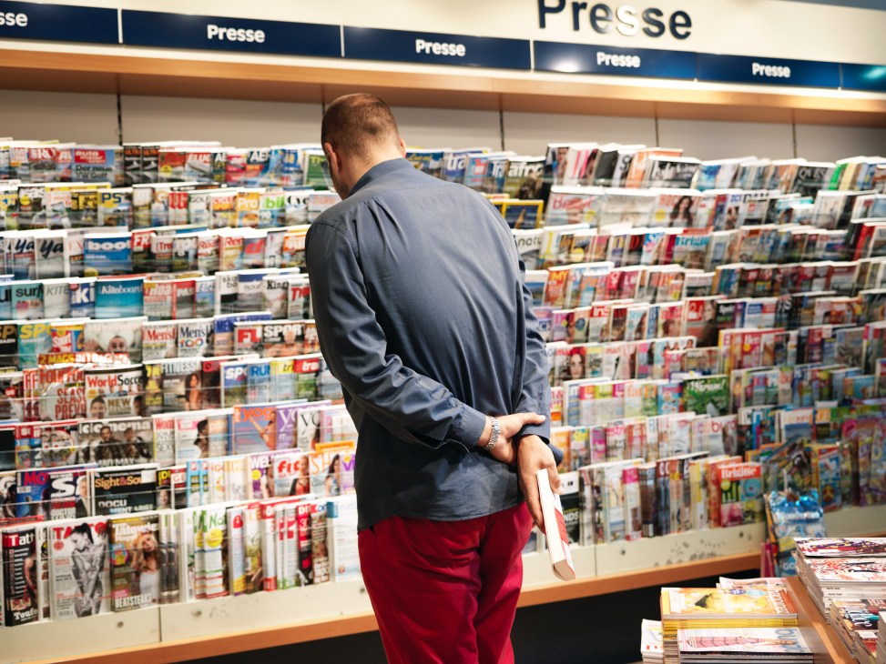 Man browsing magazines at a wall display in Thalia bookshop's press section.