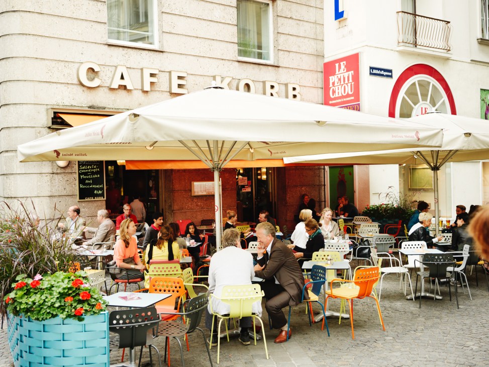Café Korb's colorful terrace with diners seated under white umbrellas on a Vienna street.